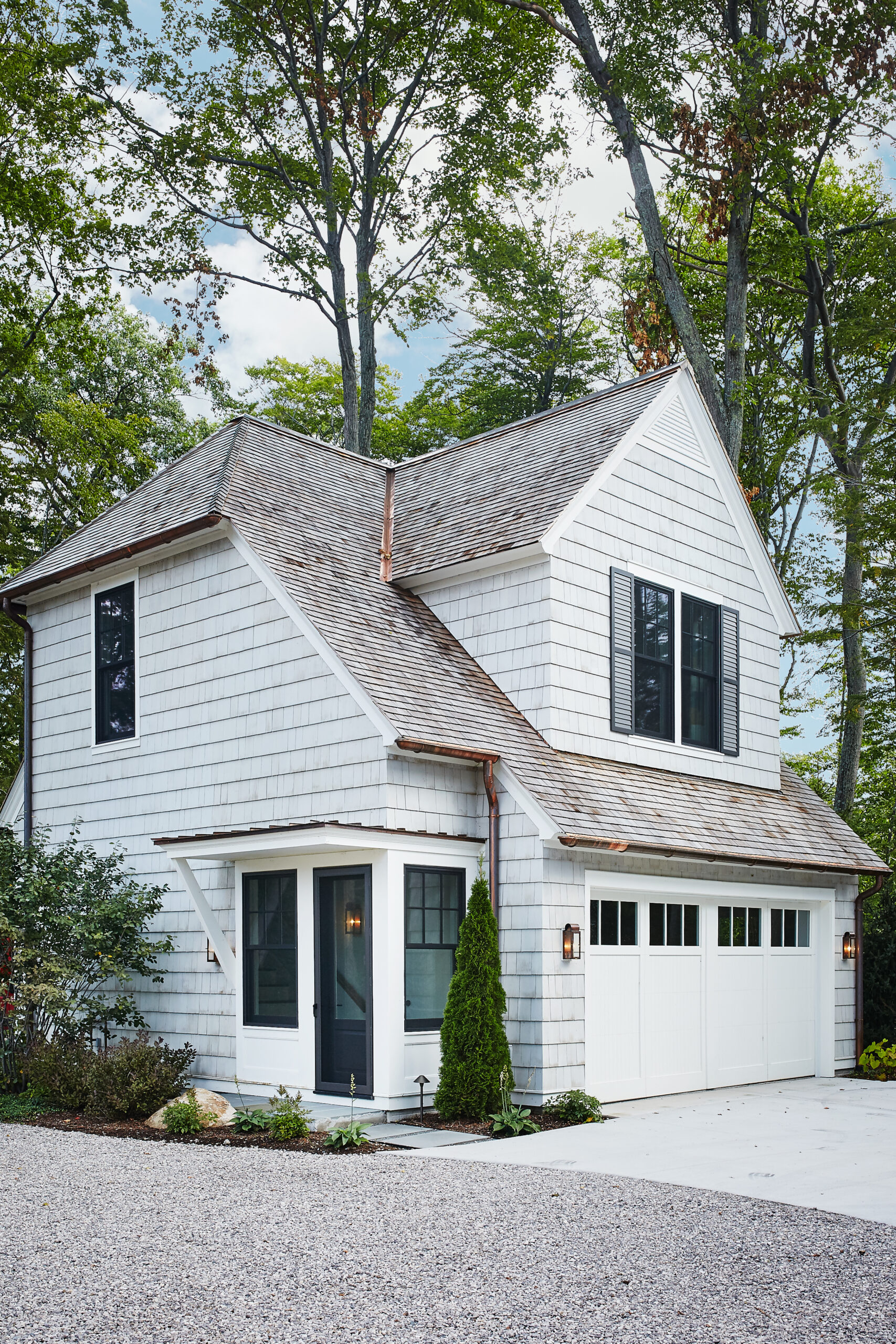 White shingle carriage house with gabled roof, garage doors, and second-story windows