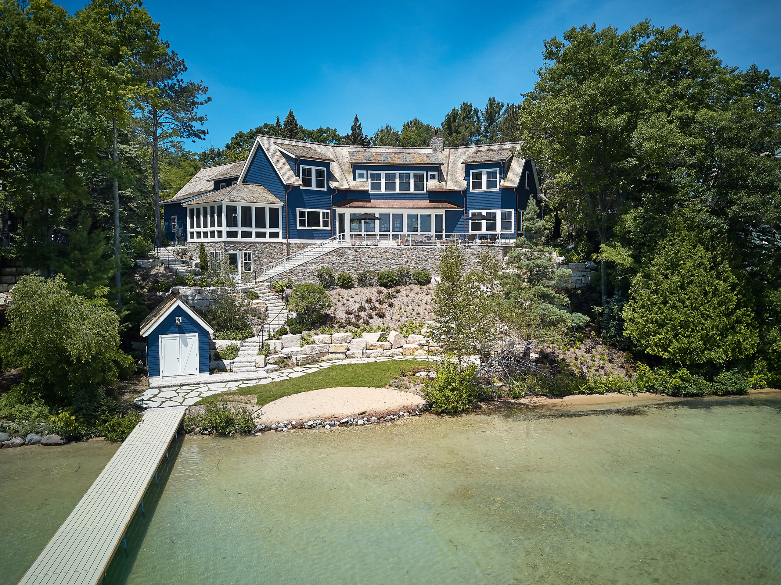 Aerial view of custom lakeside home with stone terraces, private dock, and wooded shoreline