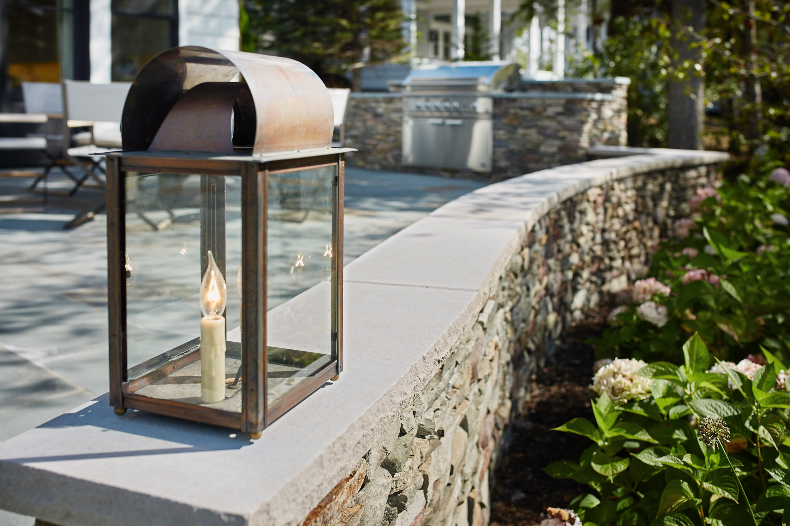 Metal lantern on stone patio wall with built-in outdoor kitchen in background