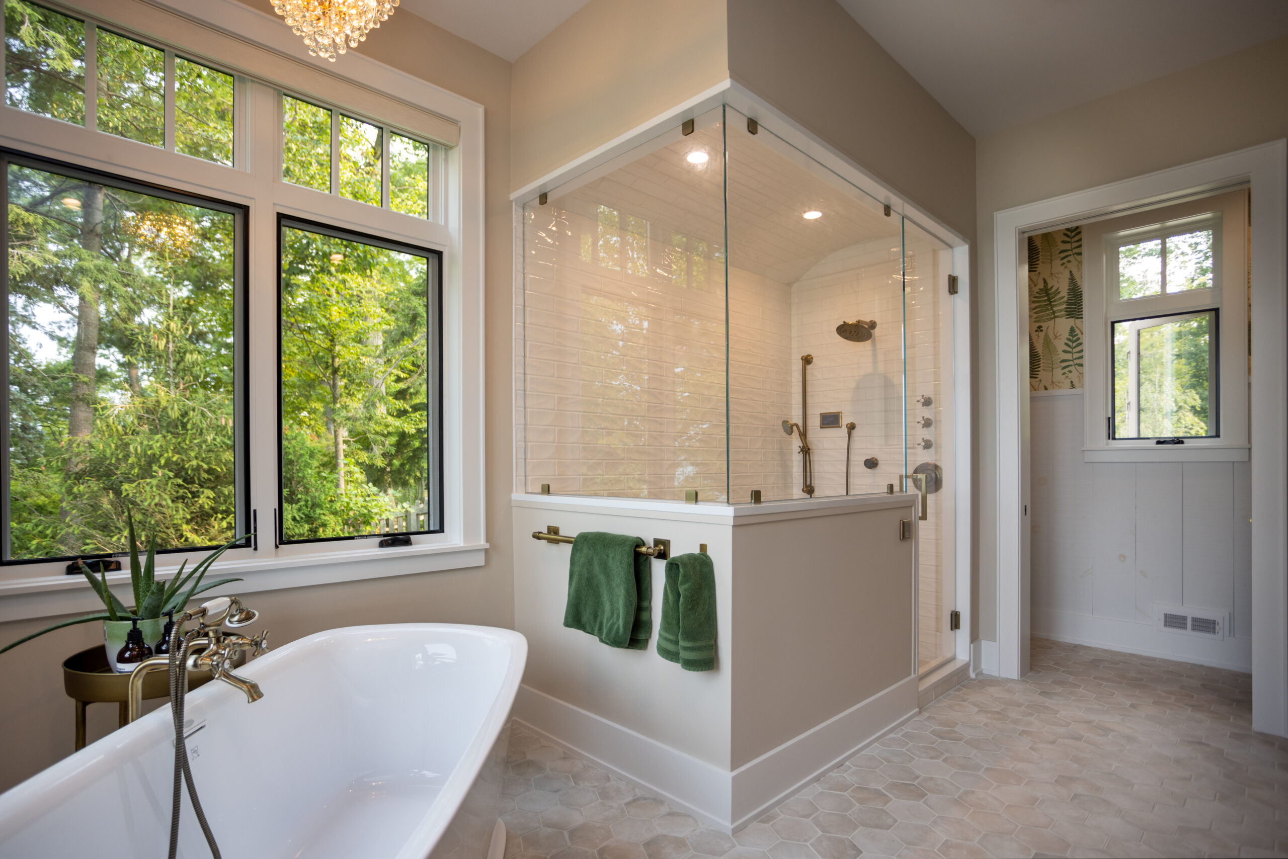 Bright bathroom with freestanding tub, walk-in shower, and forest view.