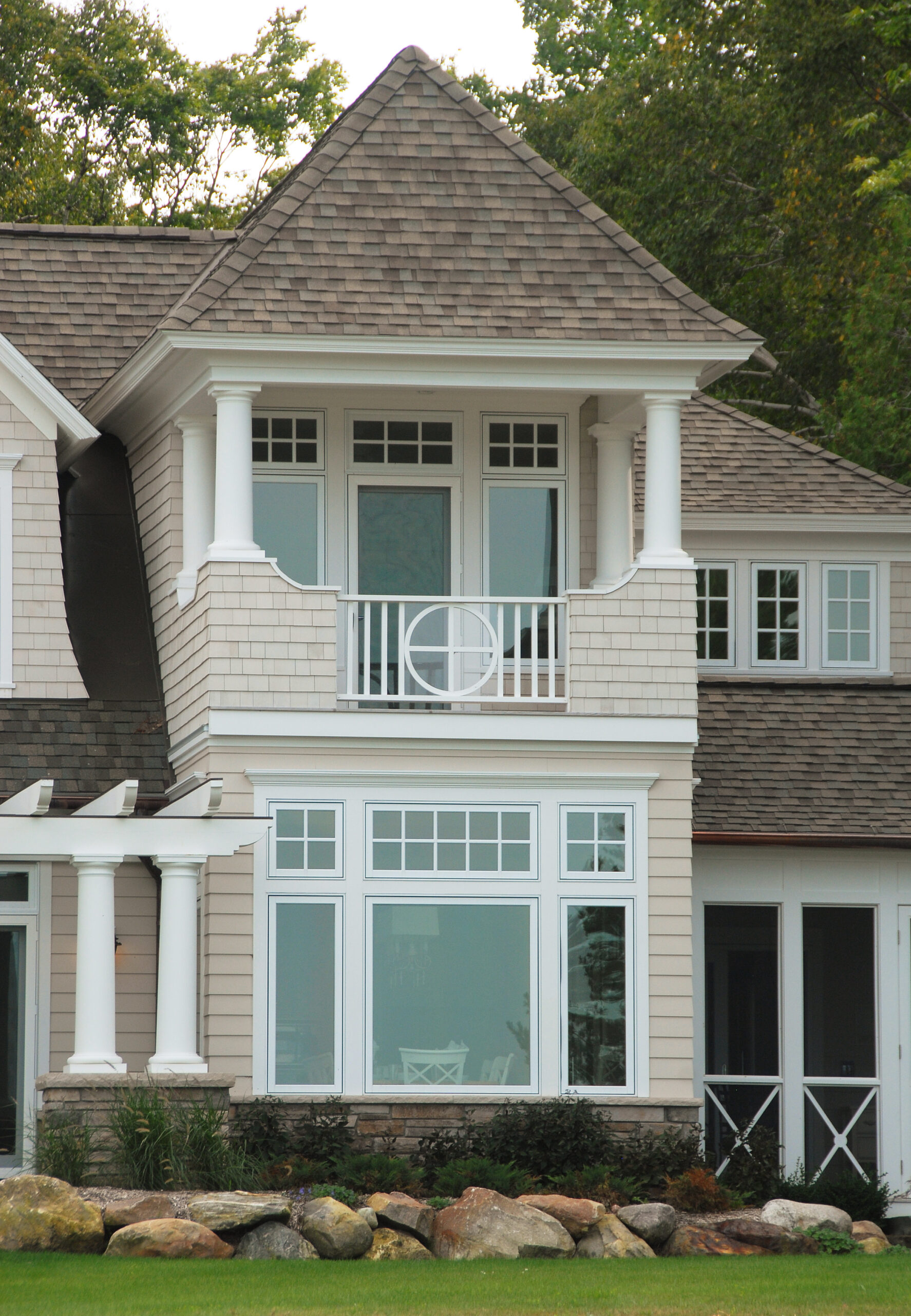 Lakeside cottage exterior with shingled facade, upper balcony, and large picture windows