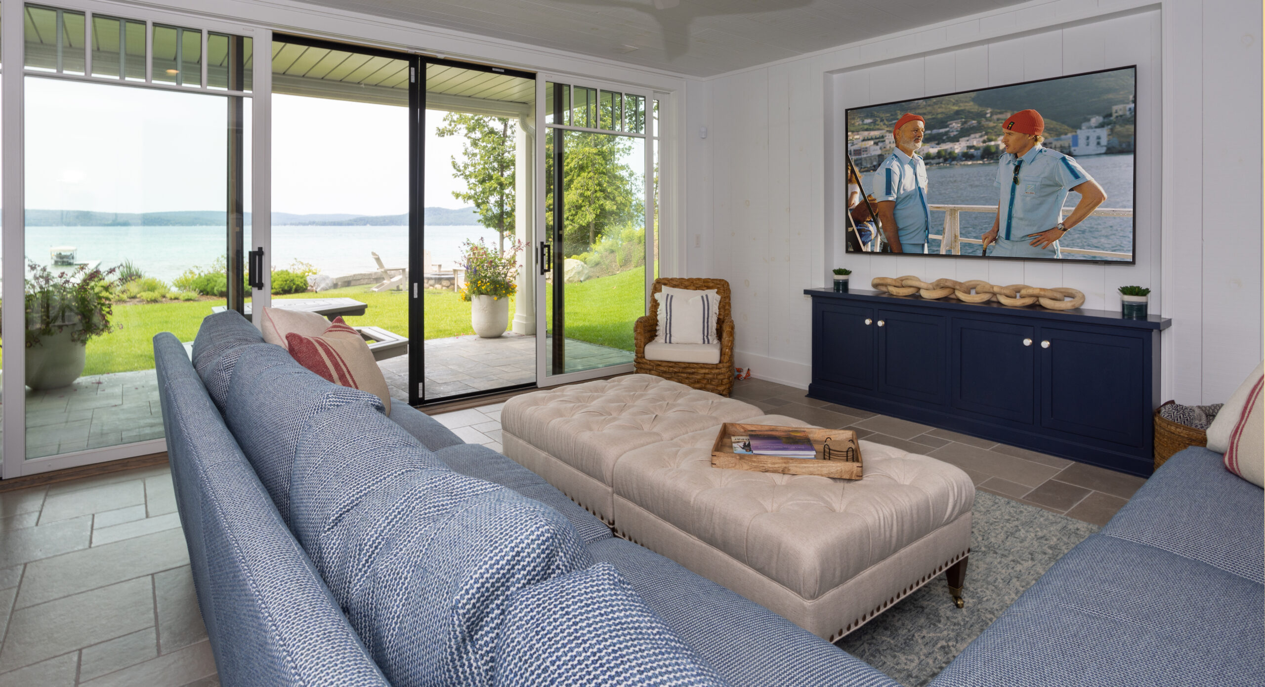 Lakeside lounge with walk-out patio, blue sofa, and large TV.