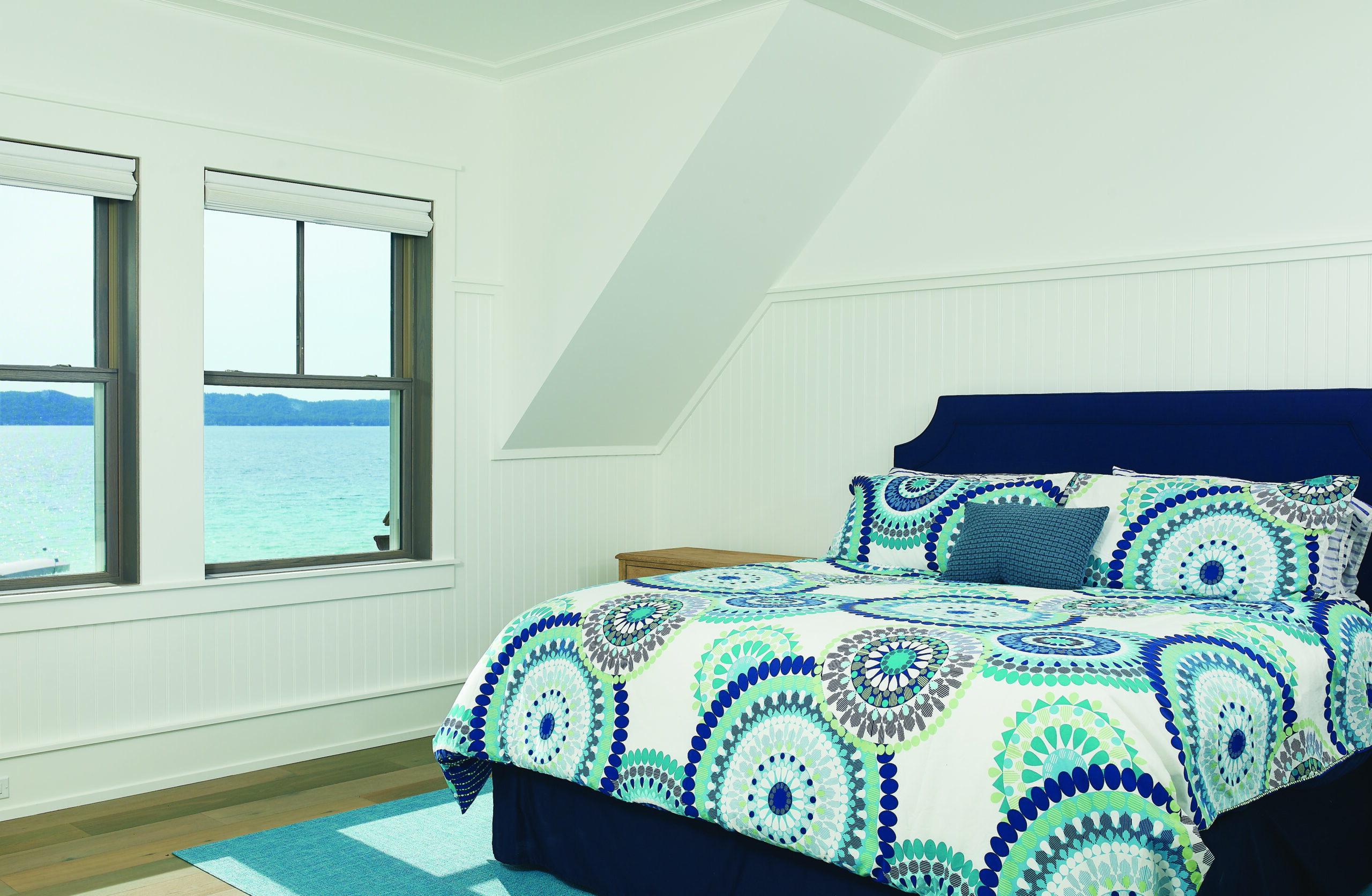 Lake-view bedroom with white shiplap walls and patterned bedding in Glen Arbor home