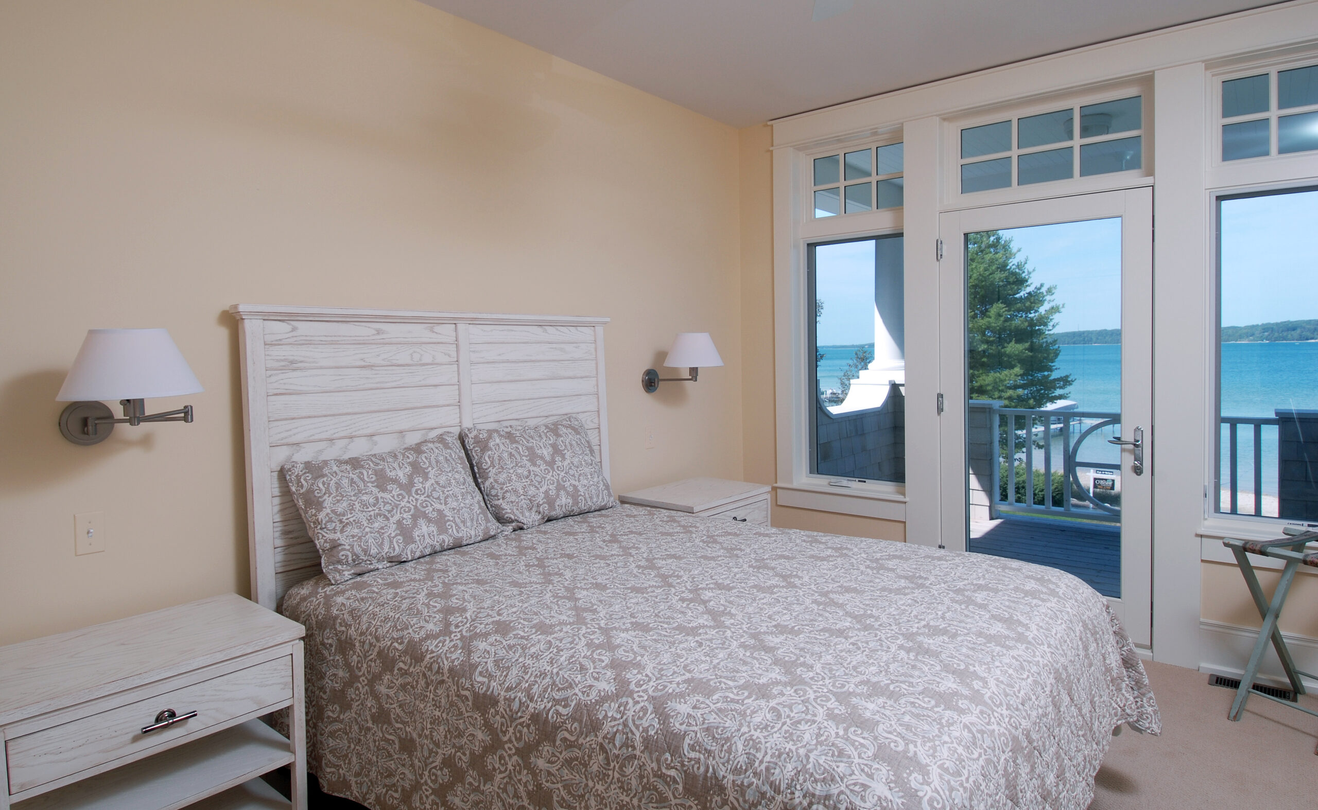 Guest bedroom with white wood bed frame and glass door opening to a lakeside balcony