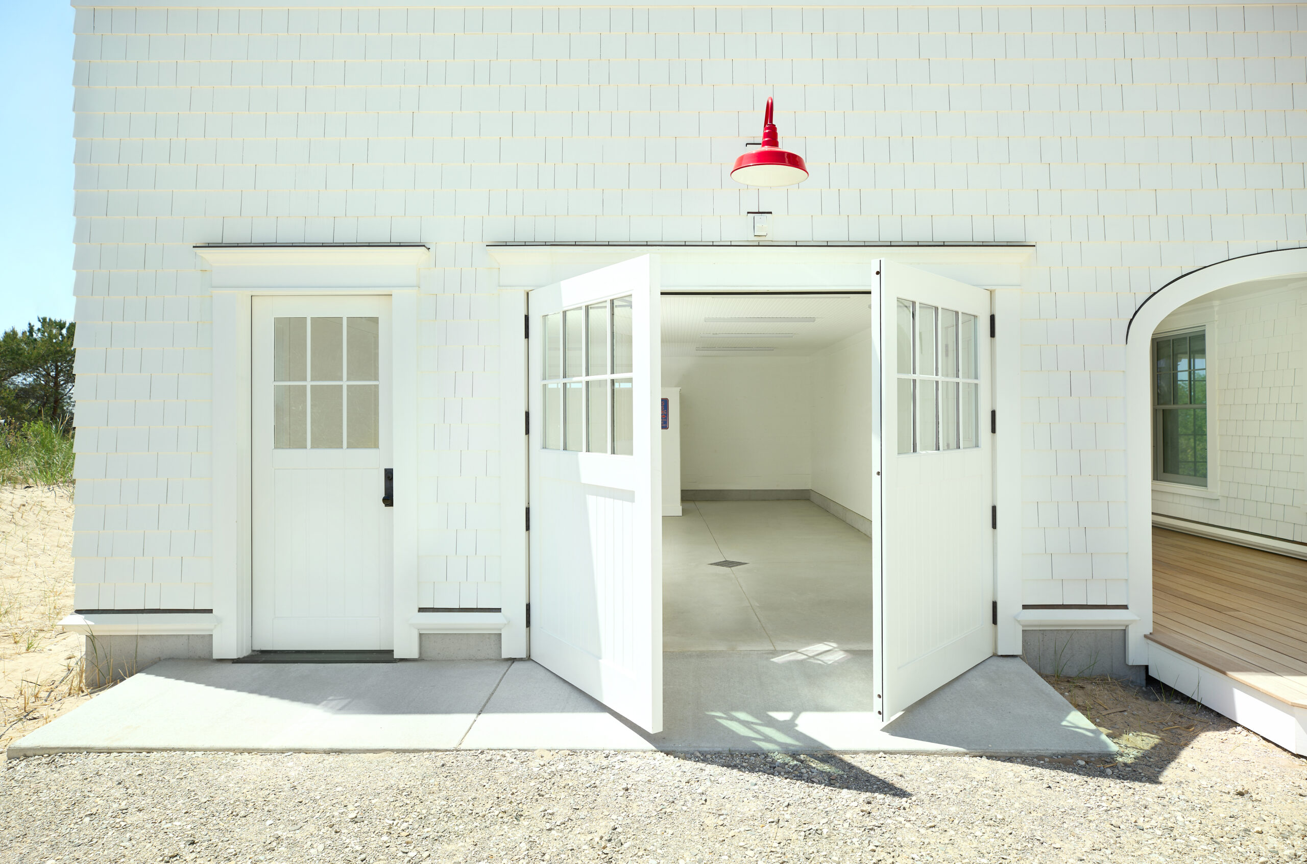 White shingle-style garage with double doors open, showing a clean interior and a red exterior light fixture above.