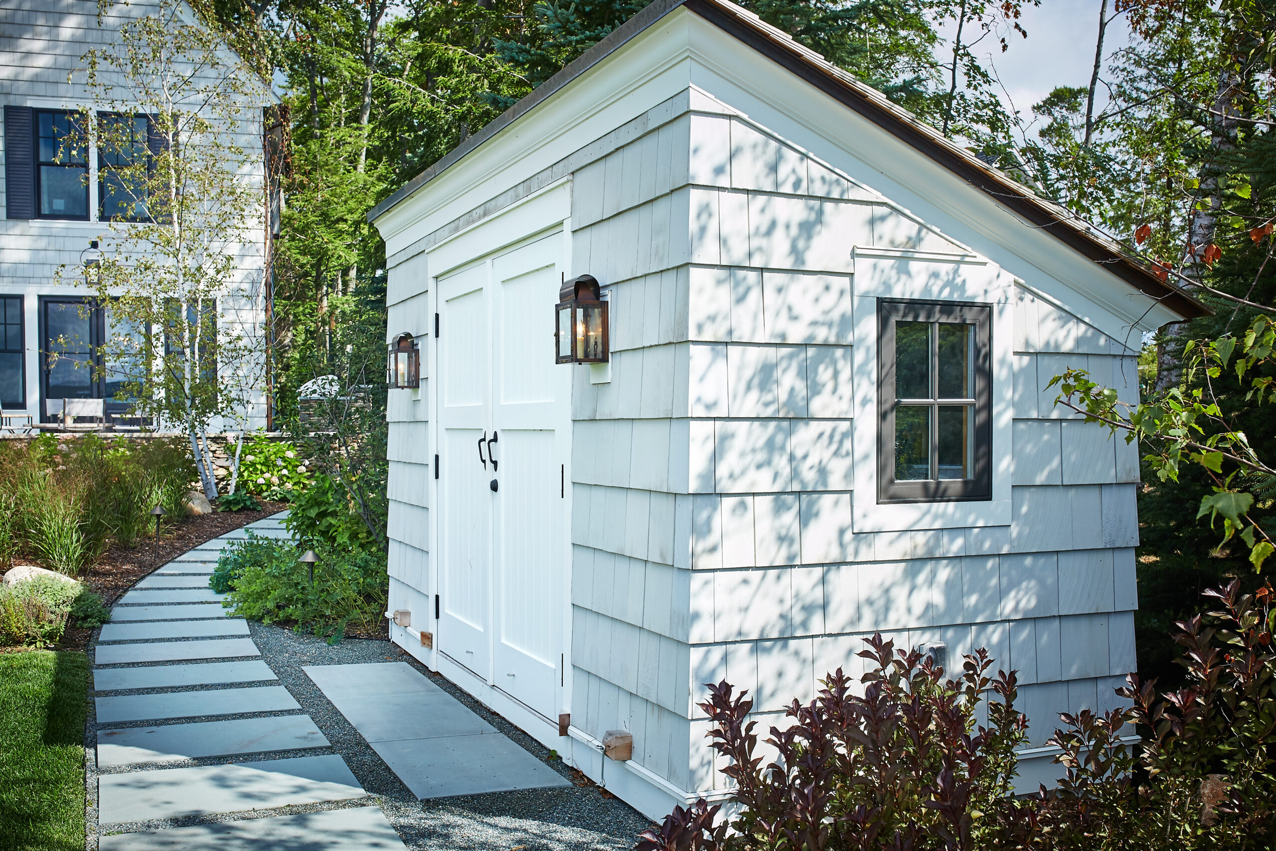 Shingle-style lakeside boathouse with double doors, lantern sconces, and stone walkway