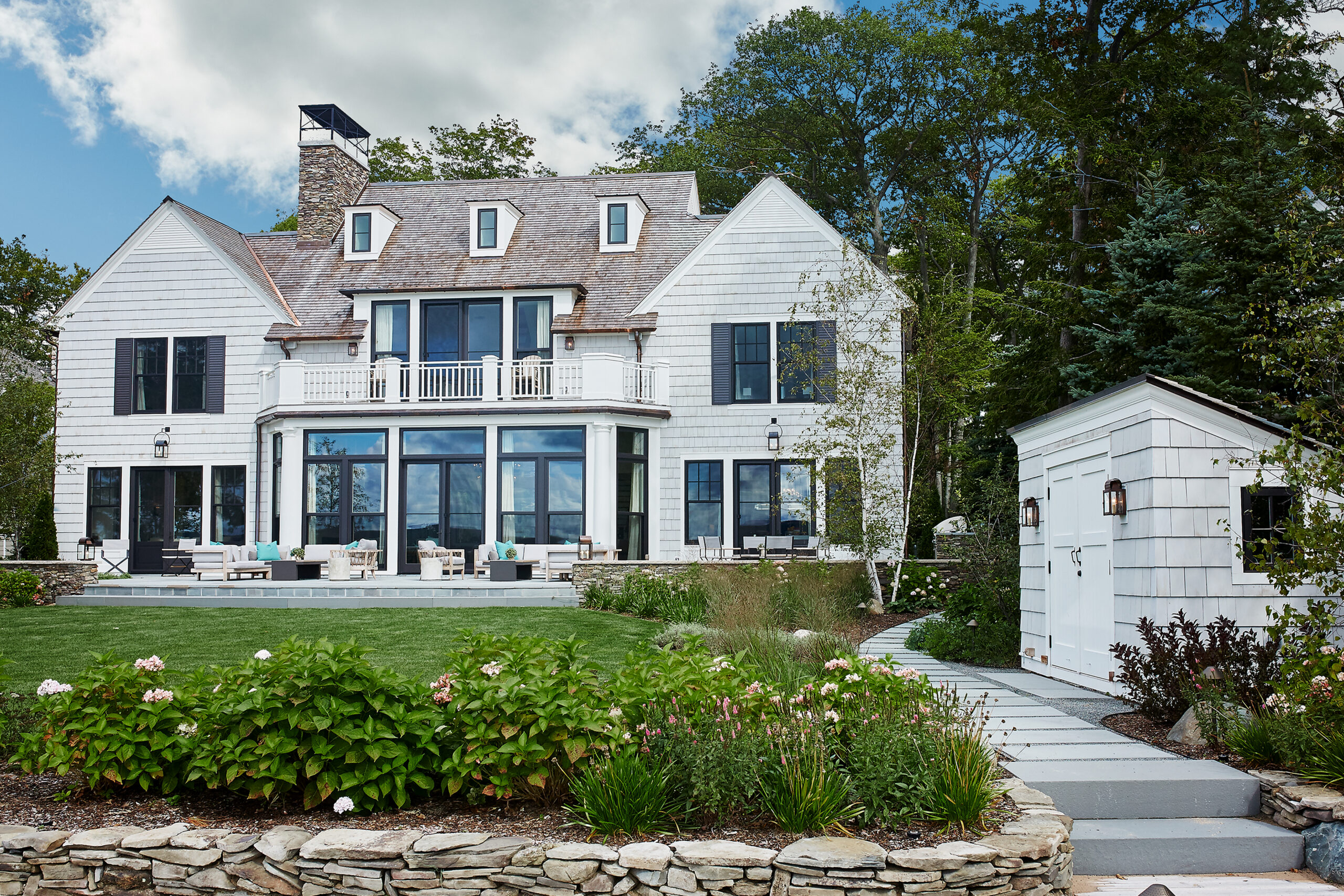 Shingle-style lakeside home with stone chimney, terraces, and landscaped grounds