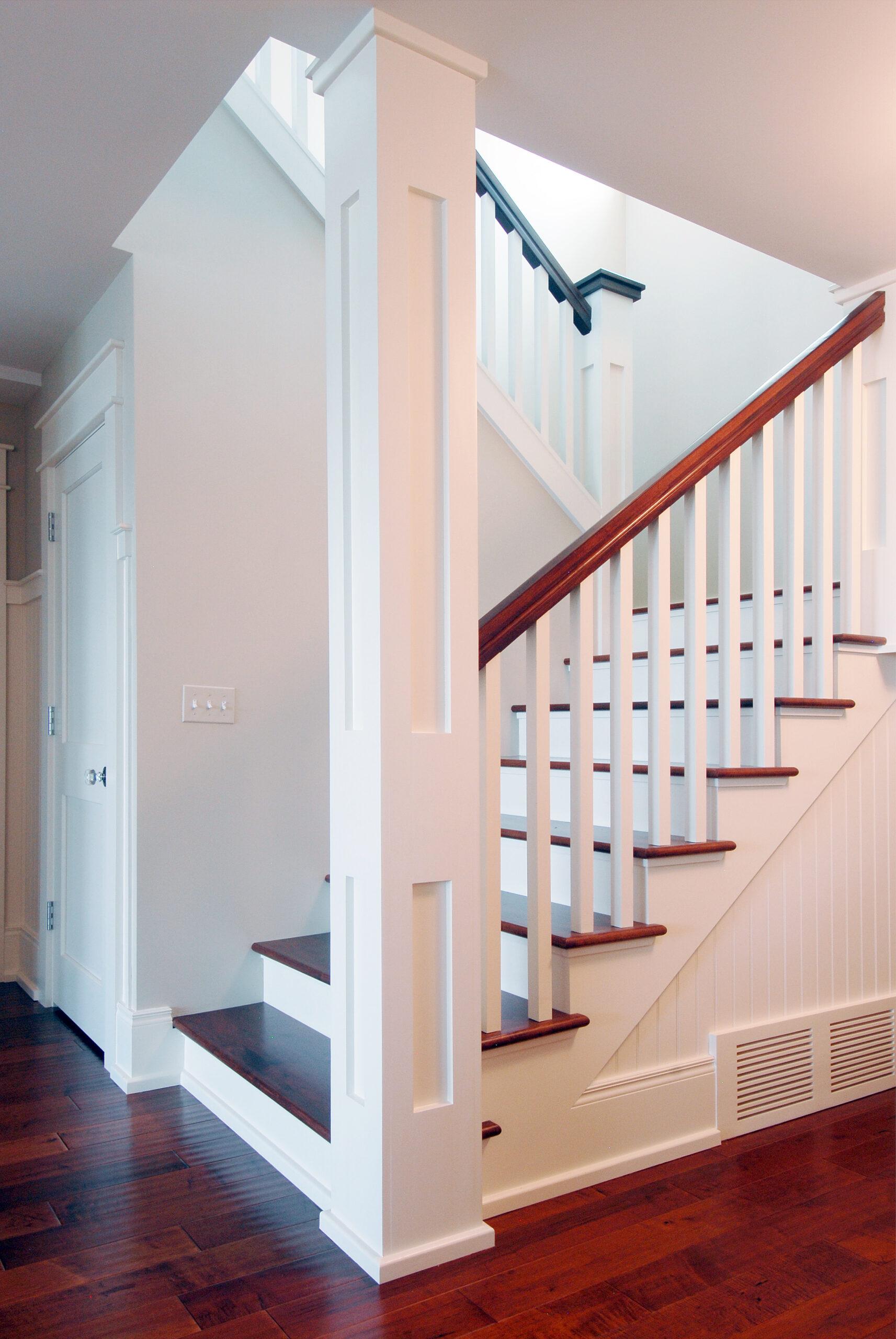 White staircase with wood treads, craftsman-style trim, and painted balusters in a coastal cottage
