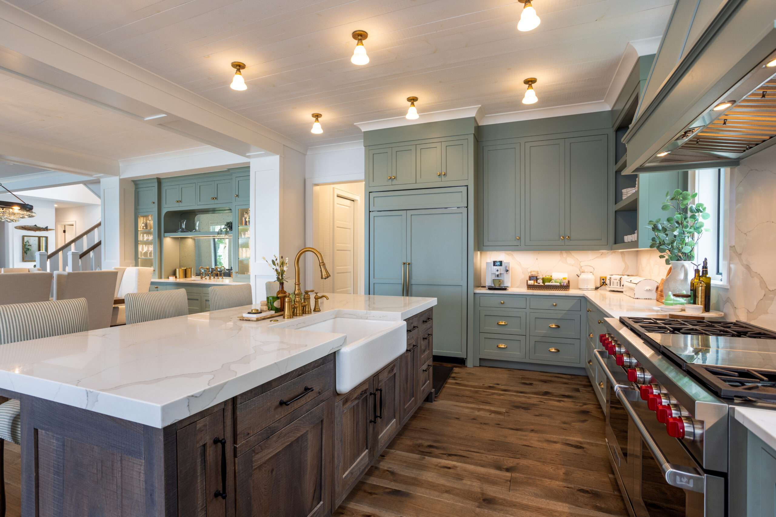 Bright gourmet kitchen with sage cabinetry, marble countertops, and brass fixtures.