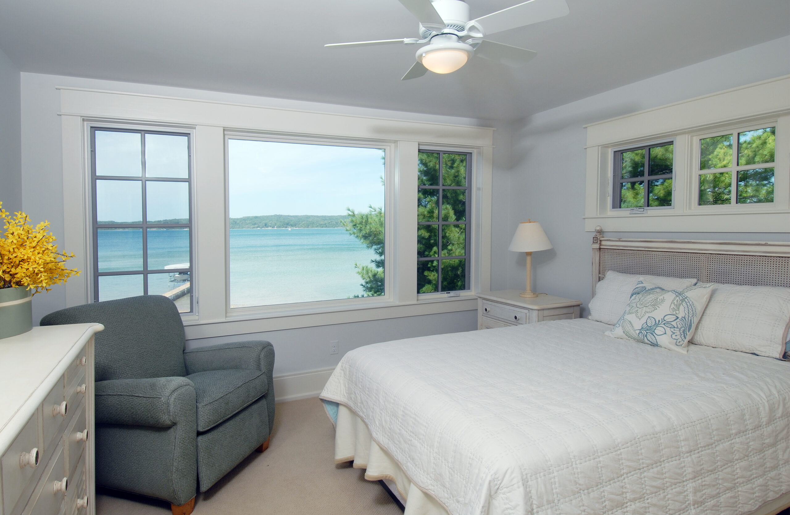 Guest bedroom with lake views, white trim windows, and a neatly made bed in a coastal cottage