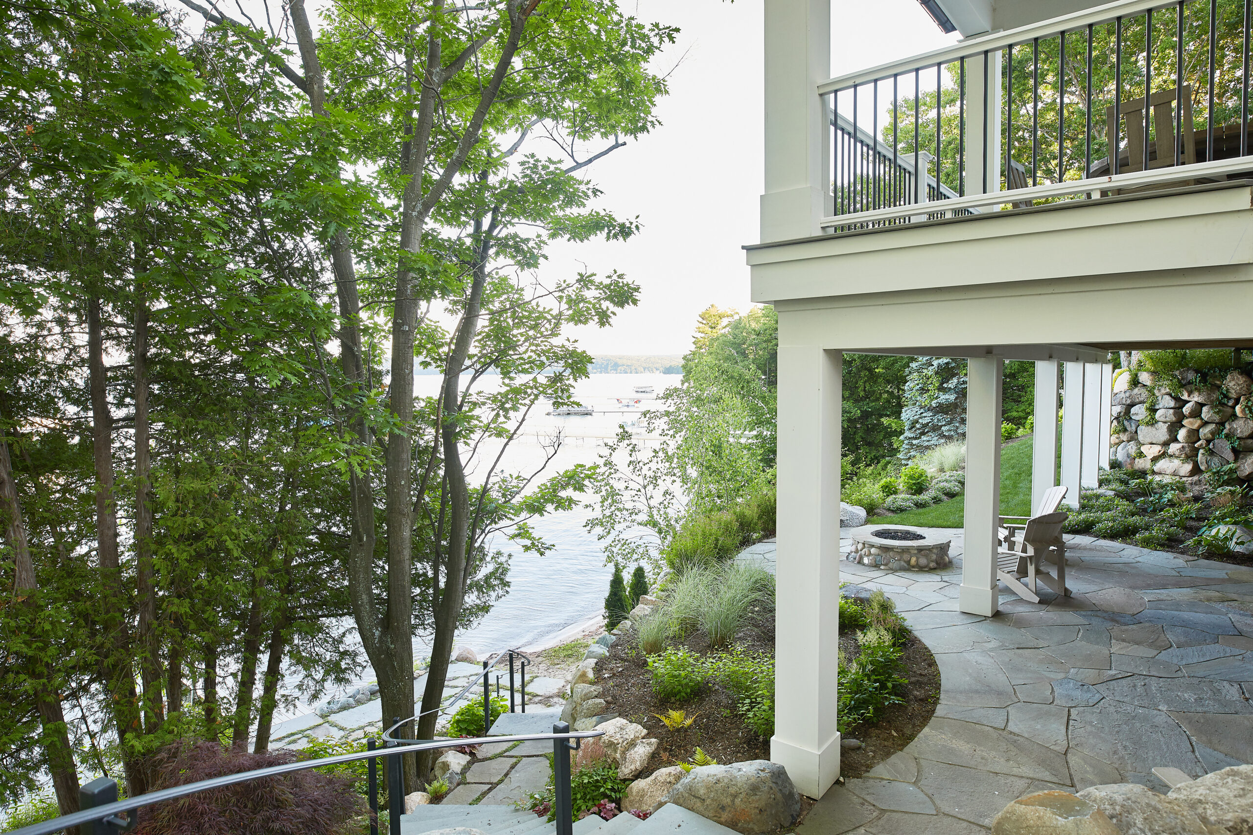 Covered lakeside patio with stone walkway and fire pit below deck