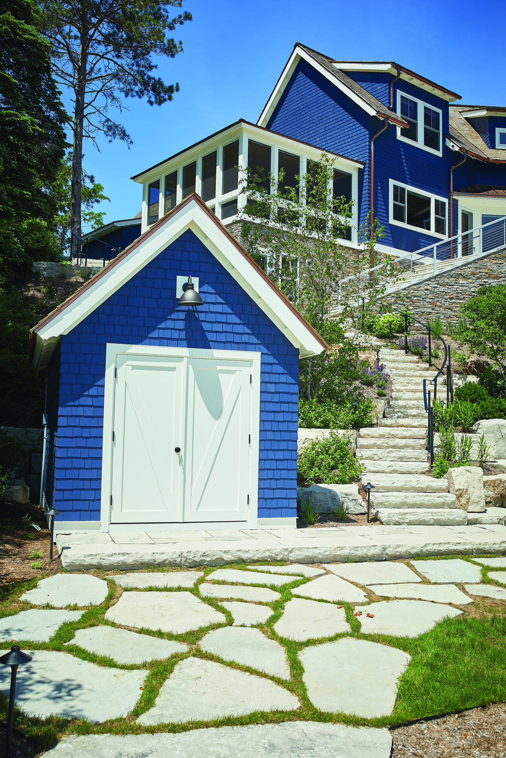 Blue shingle boathouse with white doors and stone stairway on lakeside property