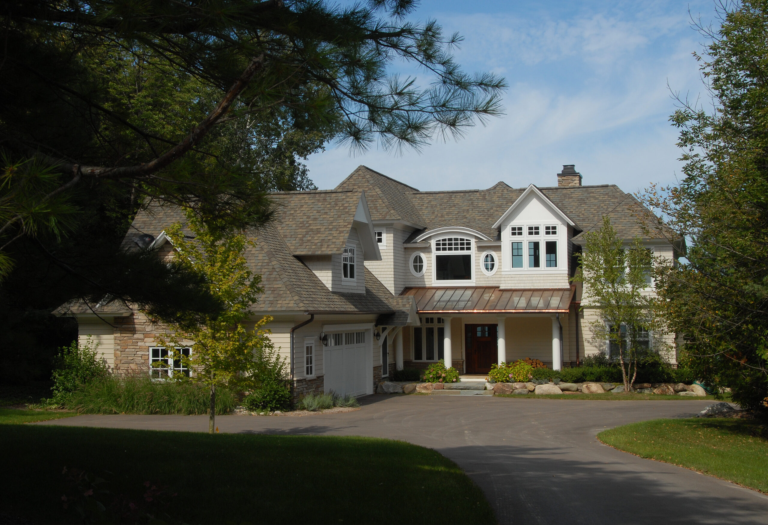Shingle-style cottage with covered entry and circular driveway surrounded by trees