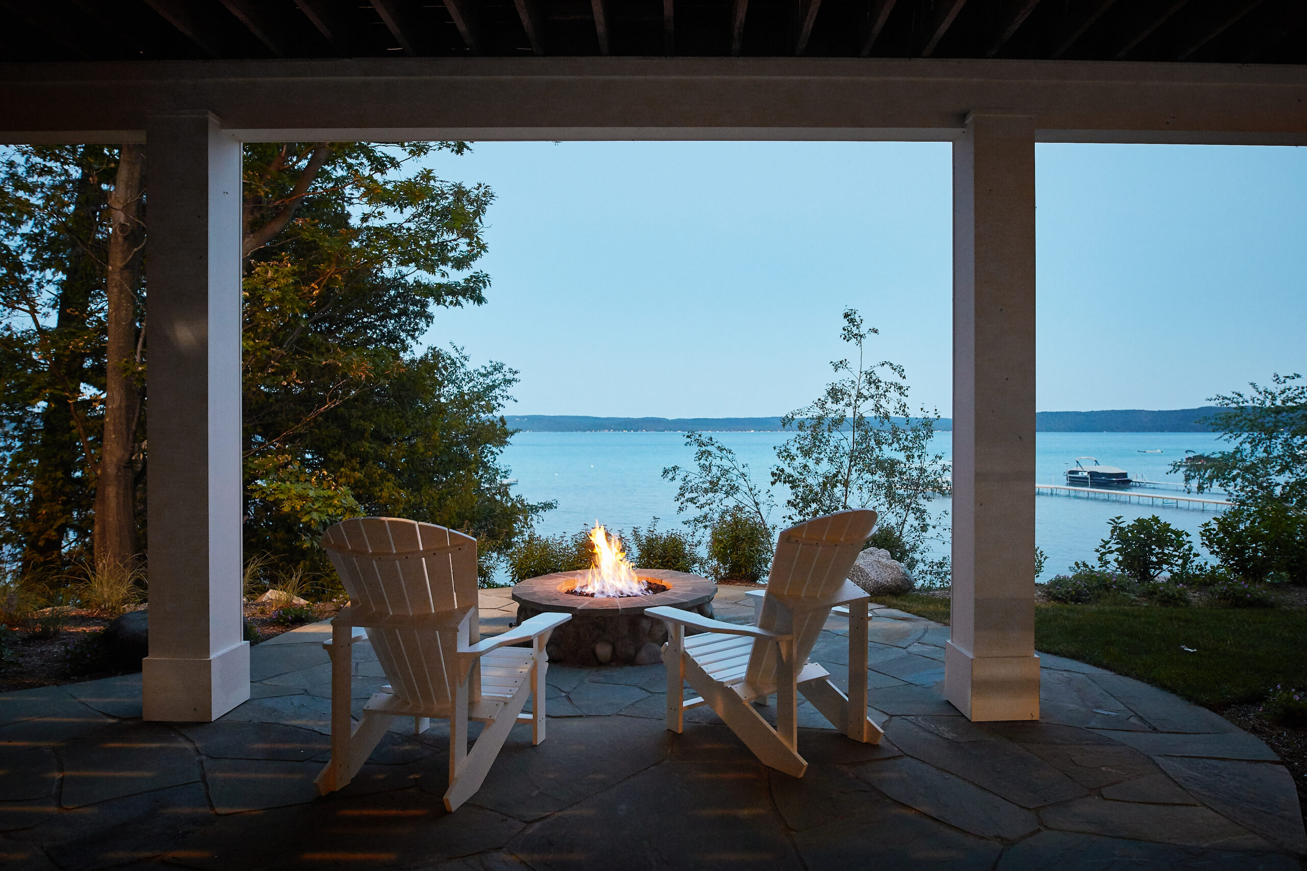 Covered lakeside patio with Adirondack chairs and fire pit at dusk