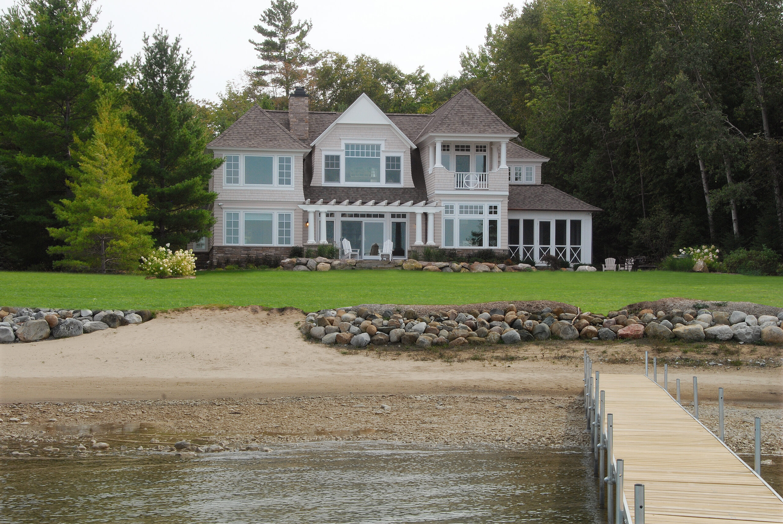 Lakeside cottage viewed from the water with dock and sandy shoreline