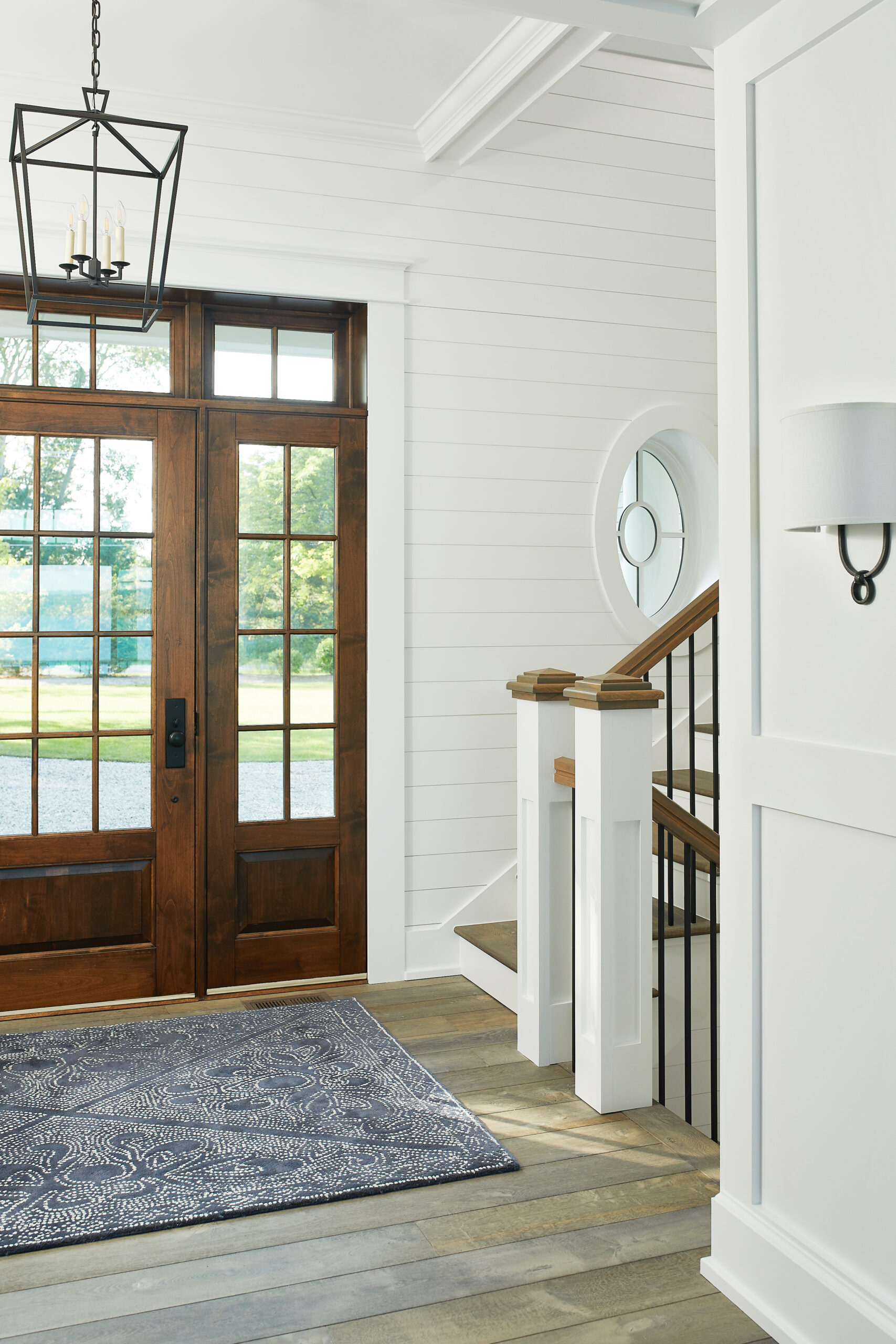 Bright entryway with wood front doors, shiplap walls, and staircase detail