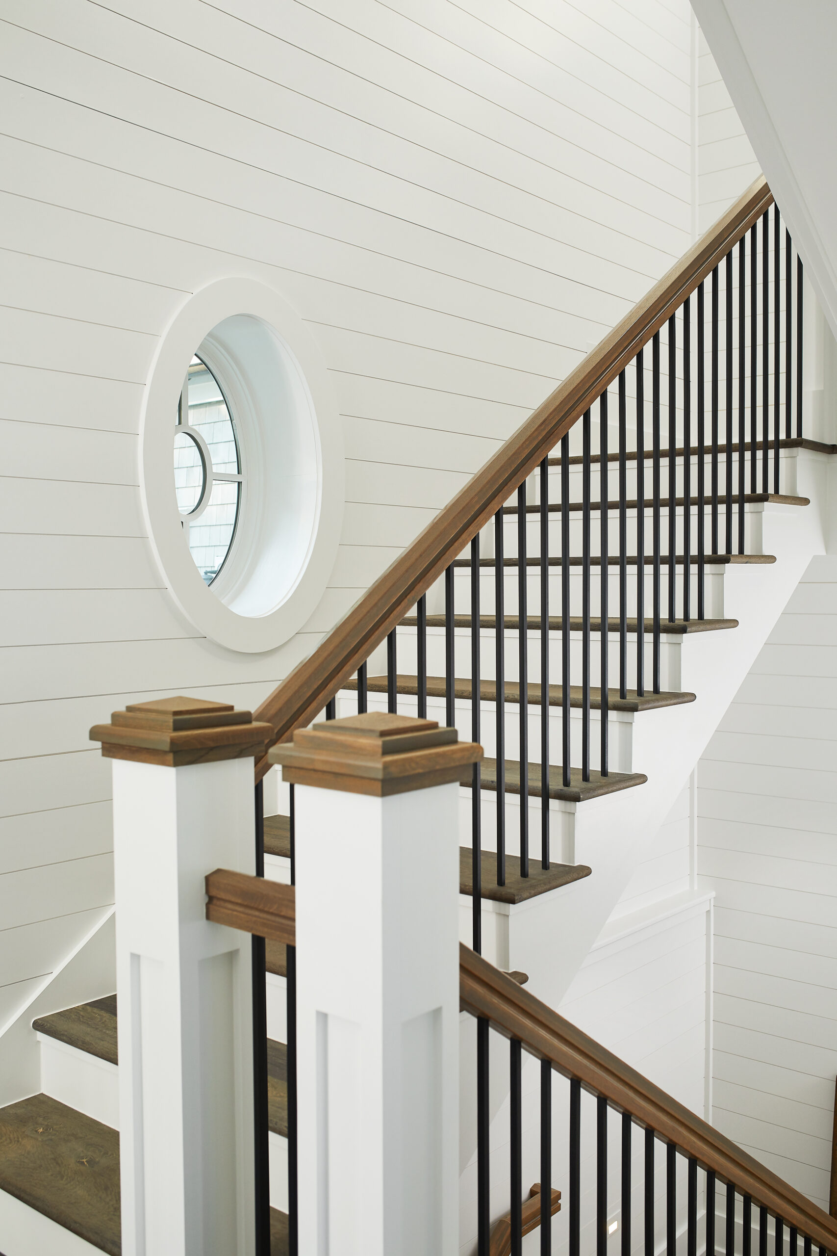 Modern interior staircase with wood treads, black balusters, and round window