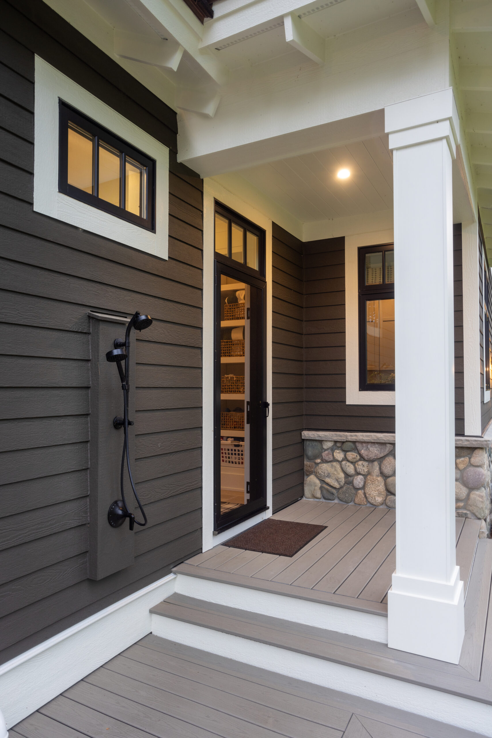 Close-up of an outdoor shower and entryway on a home with dark brown siding and stone details.