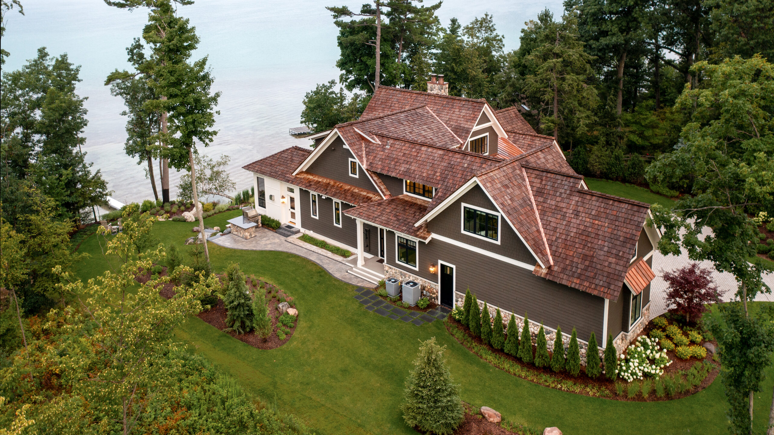 Aerial view of a brown lakefront home surrounded by trees and manicured landscaping.