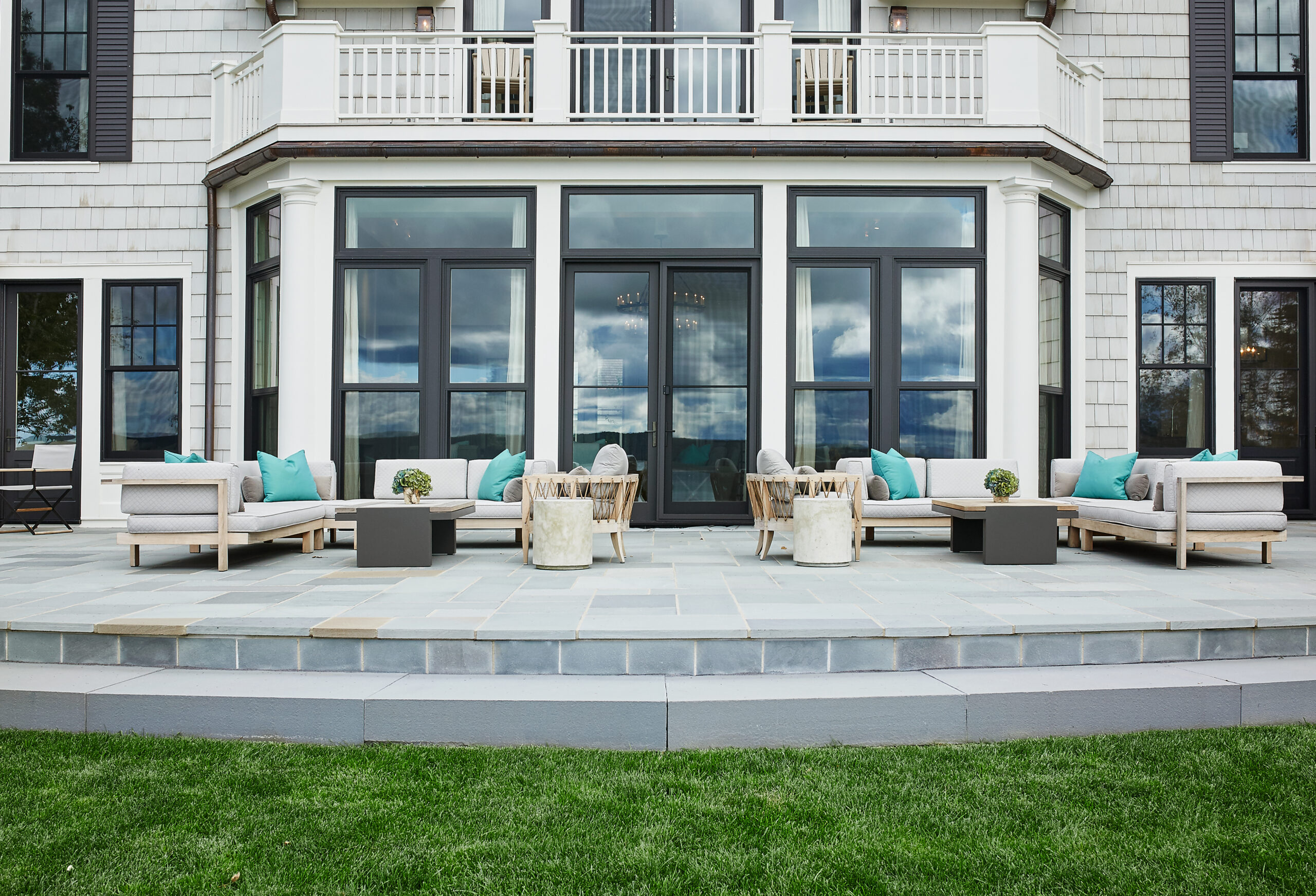 Symmetrical stone patio with outdoor seating in front of large black-framed doors