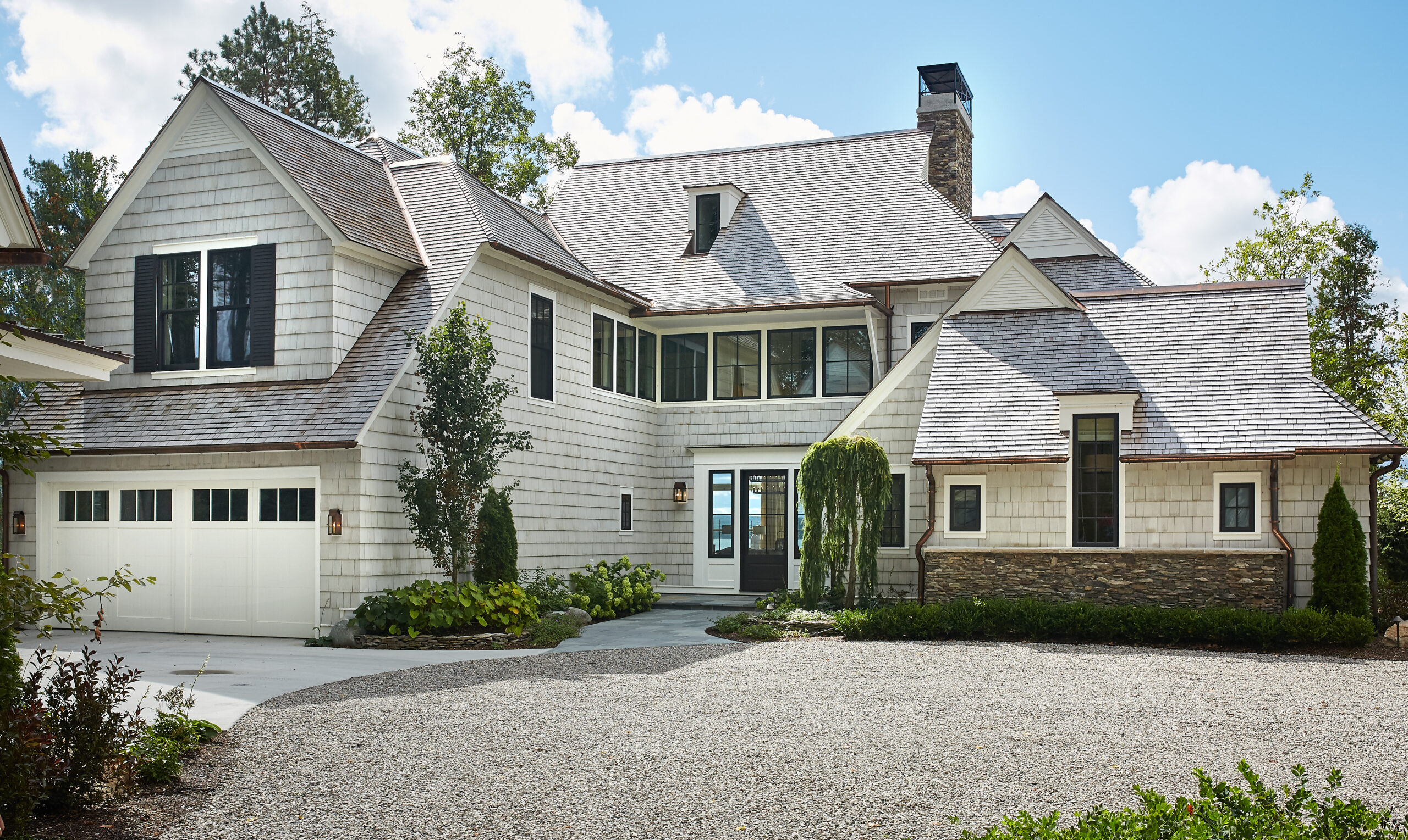 White shingle lakeside home with gabled roof, stone chimney, and attached garage