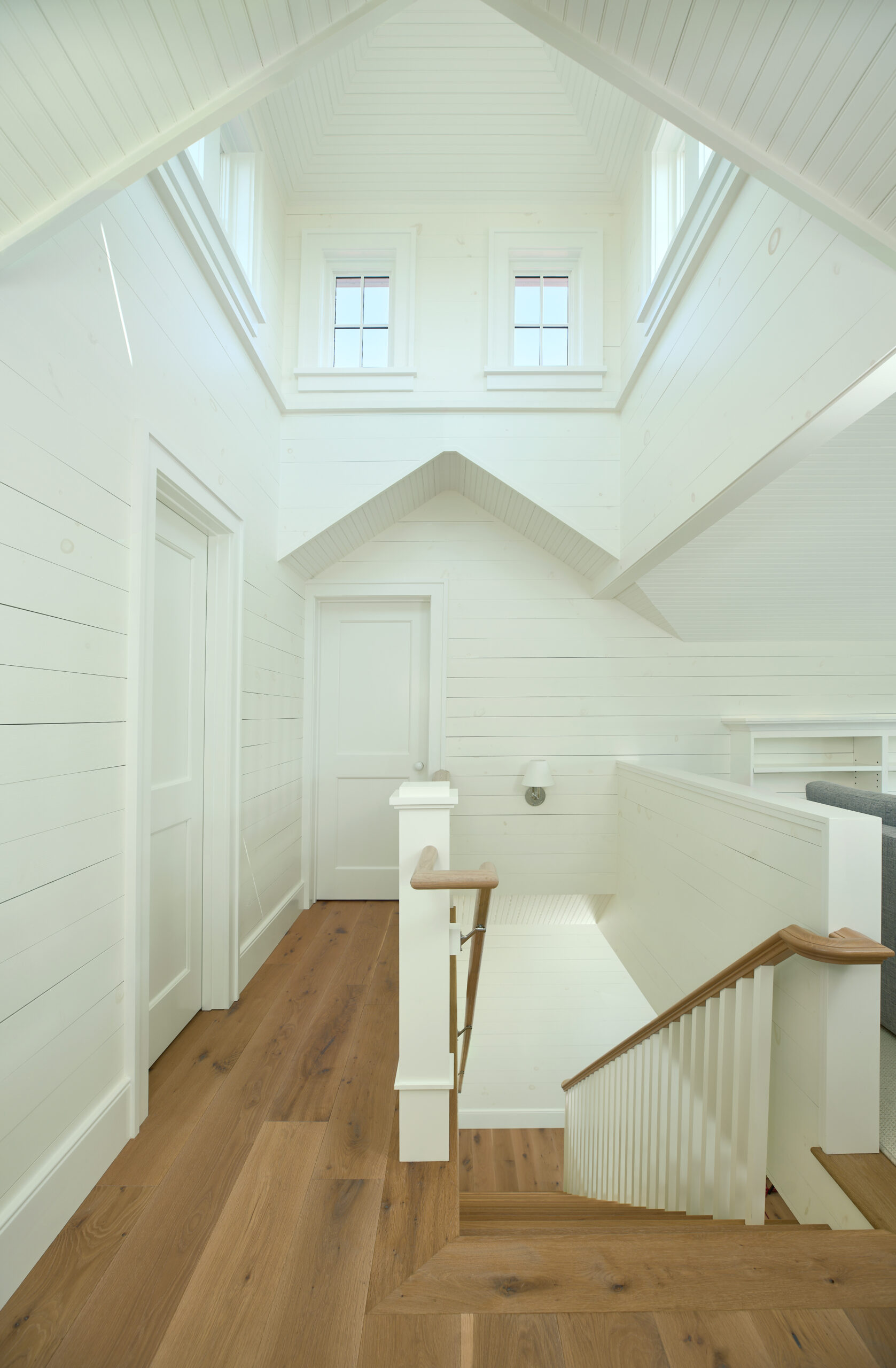 Upper landing and stairwell of Point Betsie Cottage with clerestory windows, painted wood paneling, and natural oak floors.