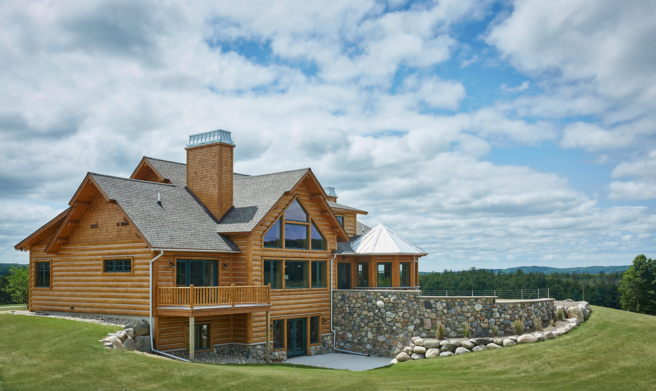 Custom log home exterior with stone terrace overlooking rolling landscape