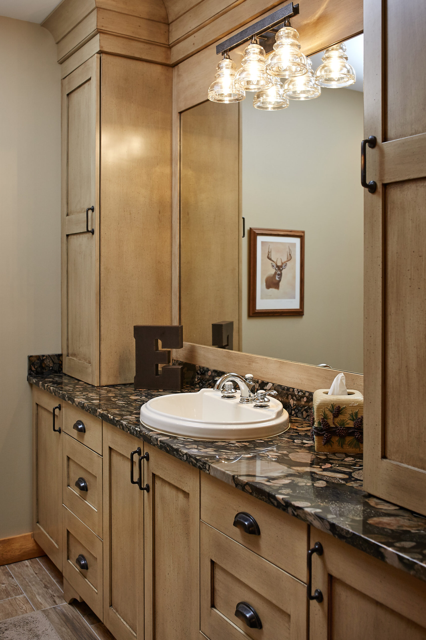 Rustic bathroom vanity with wood cabinetry, stone countertop, and glass light fixtures