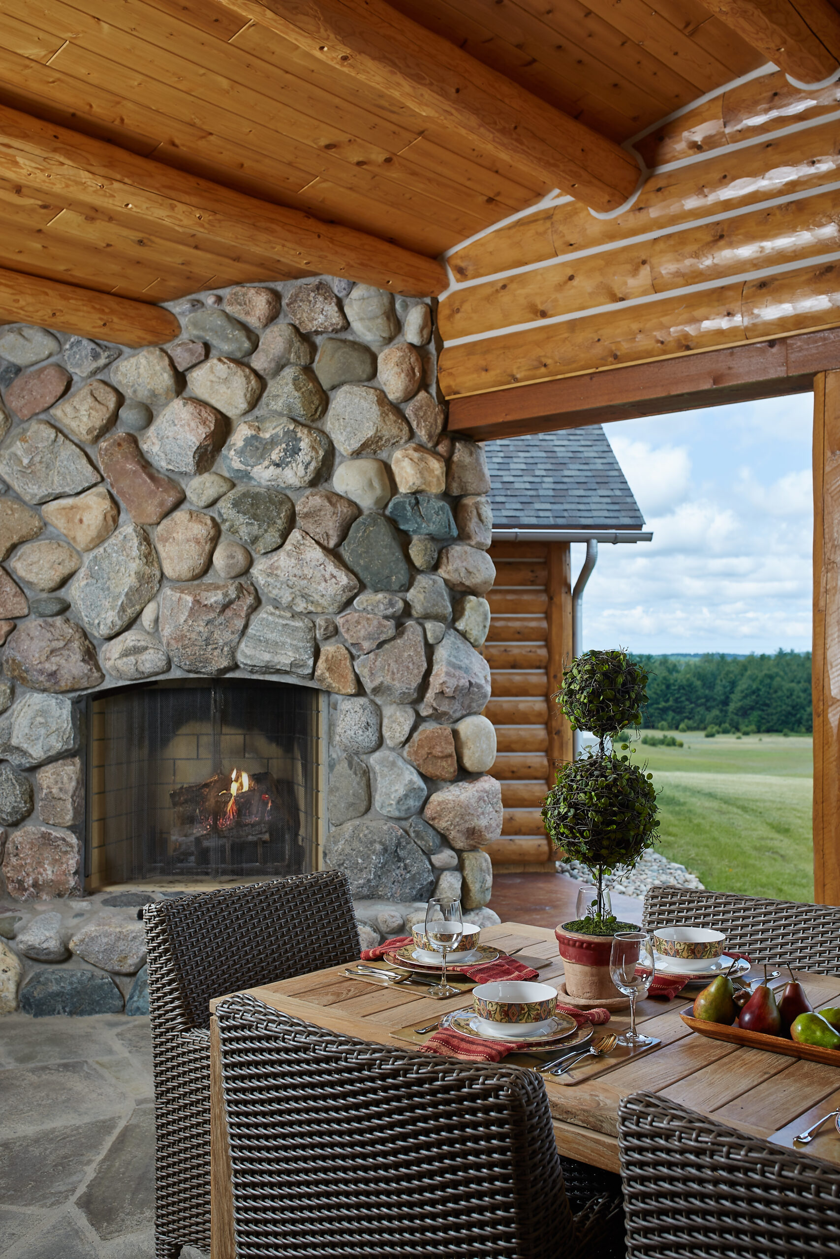 Covered outdoor dining area with stone fireplace at log cabin