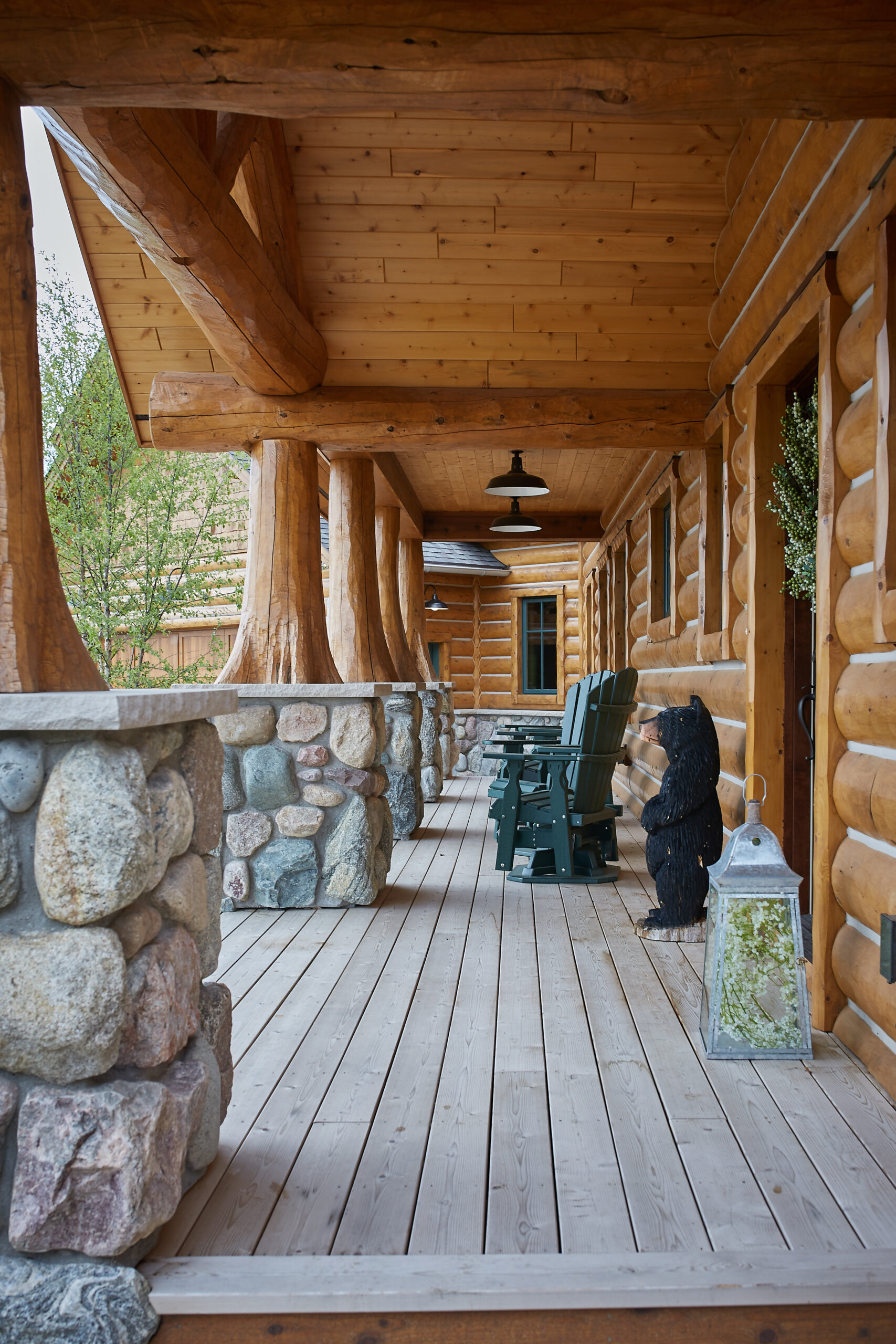 Covered log cabin porch with stone railing and Adirondack chairs