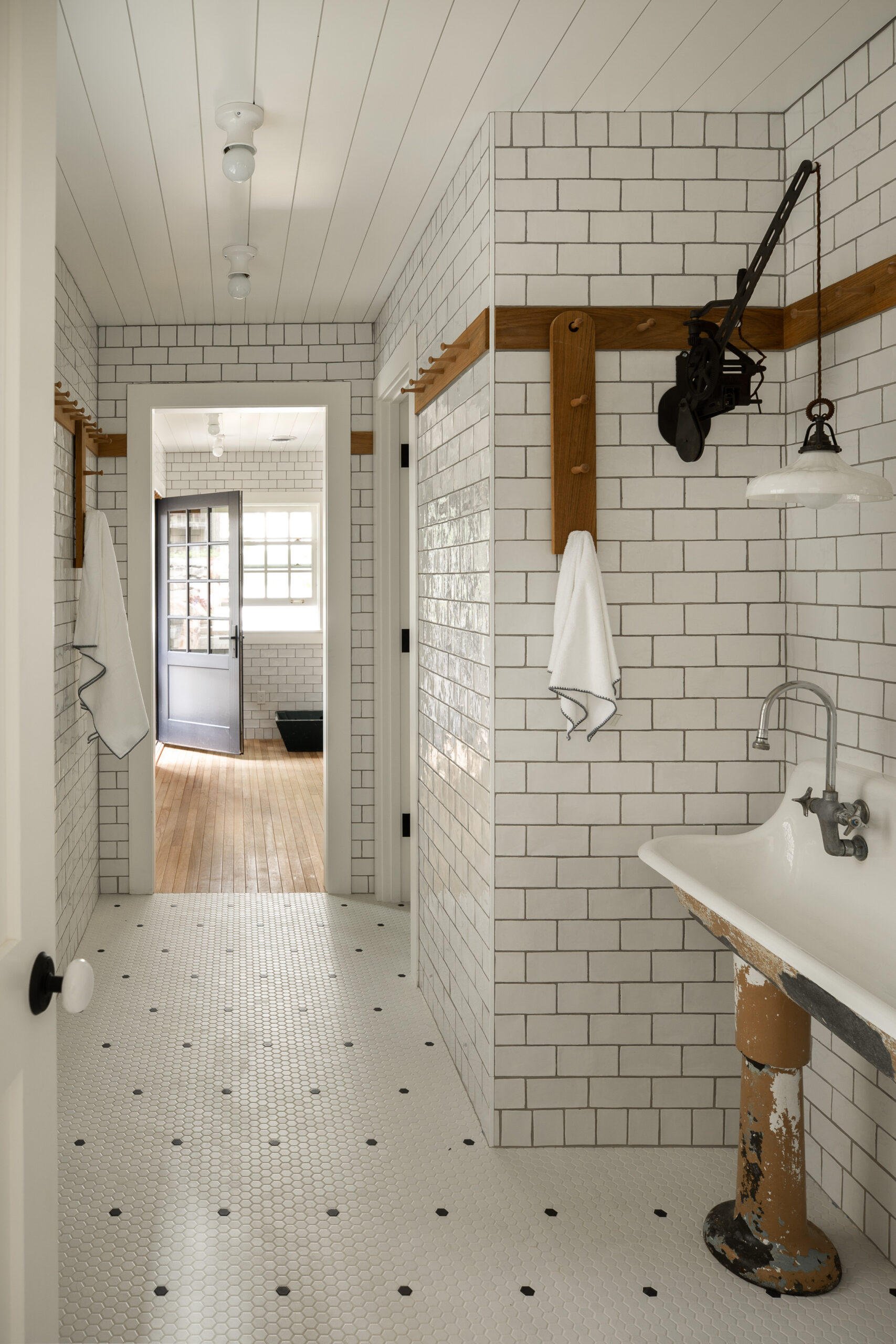 White subway-tiled bathroom hallway with vintage pedestal sink, hex tile floor, and wood accents
