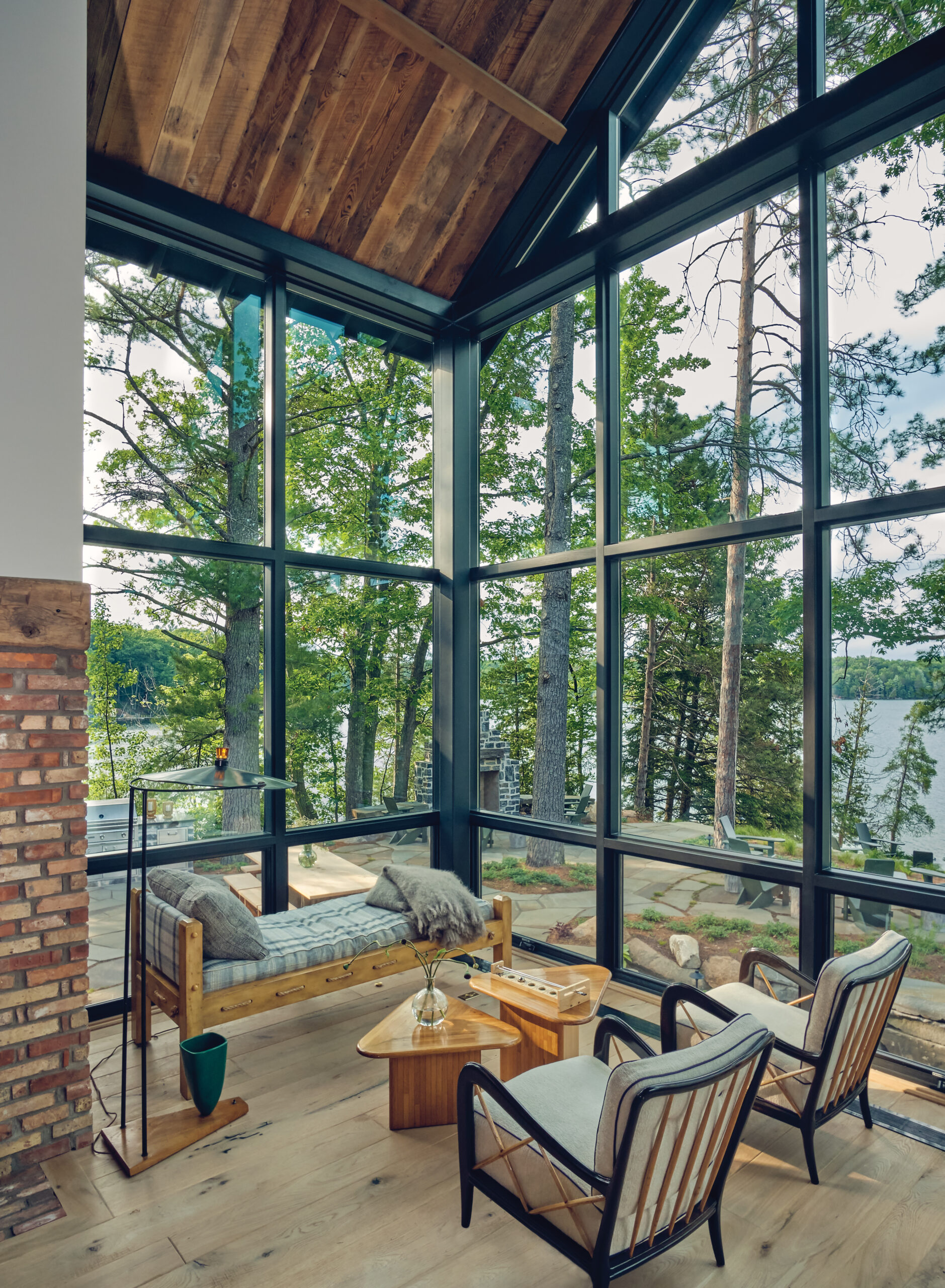 Interior sitting area with large corner windows overlooking Spider Lake, surrounded by tall trees.
