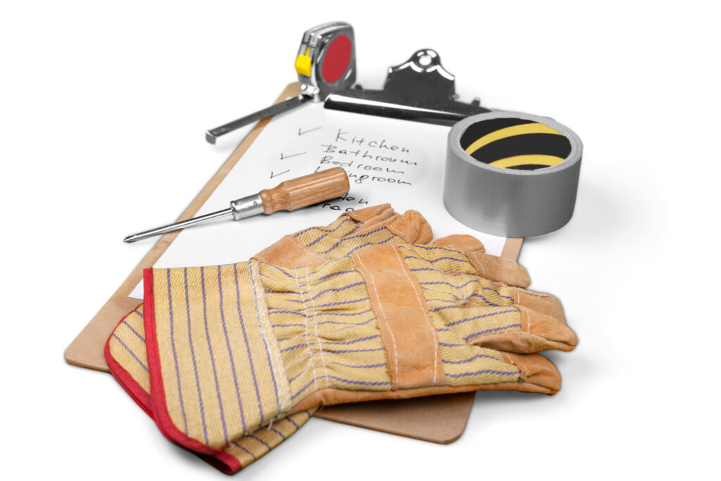 Home maintenance tools including work gloves, screwdriver, tape measure, and duct tape placed on a clipboard with a handwritten task checklist.