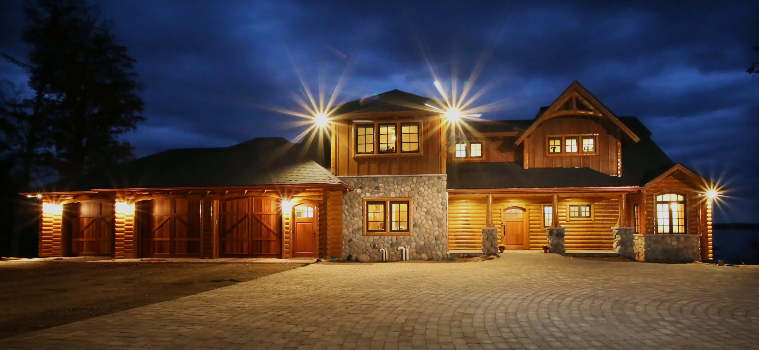 Rustic log and stone lakefront home illuminated at night.