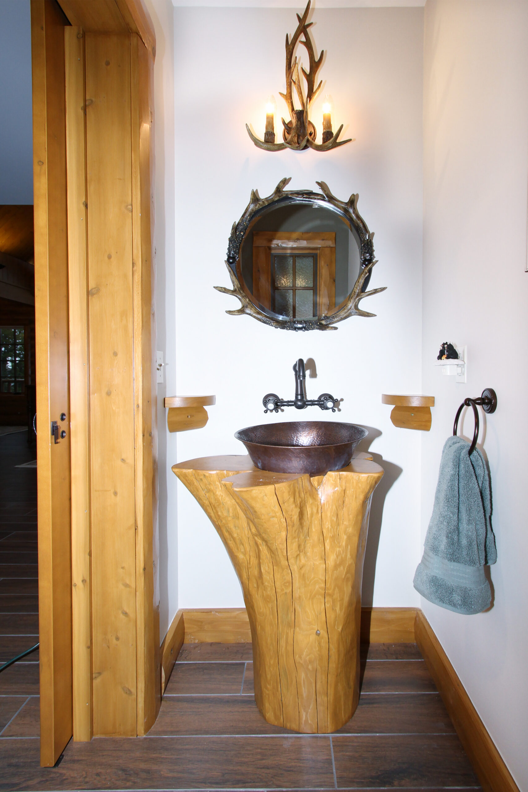 Rustic powder bath with antler mirror and a tree-stump vanity.