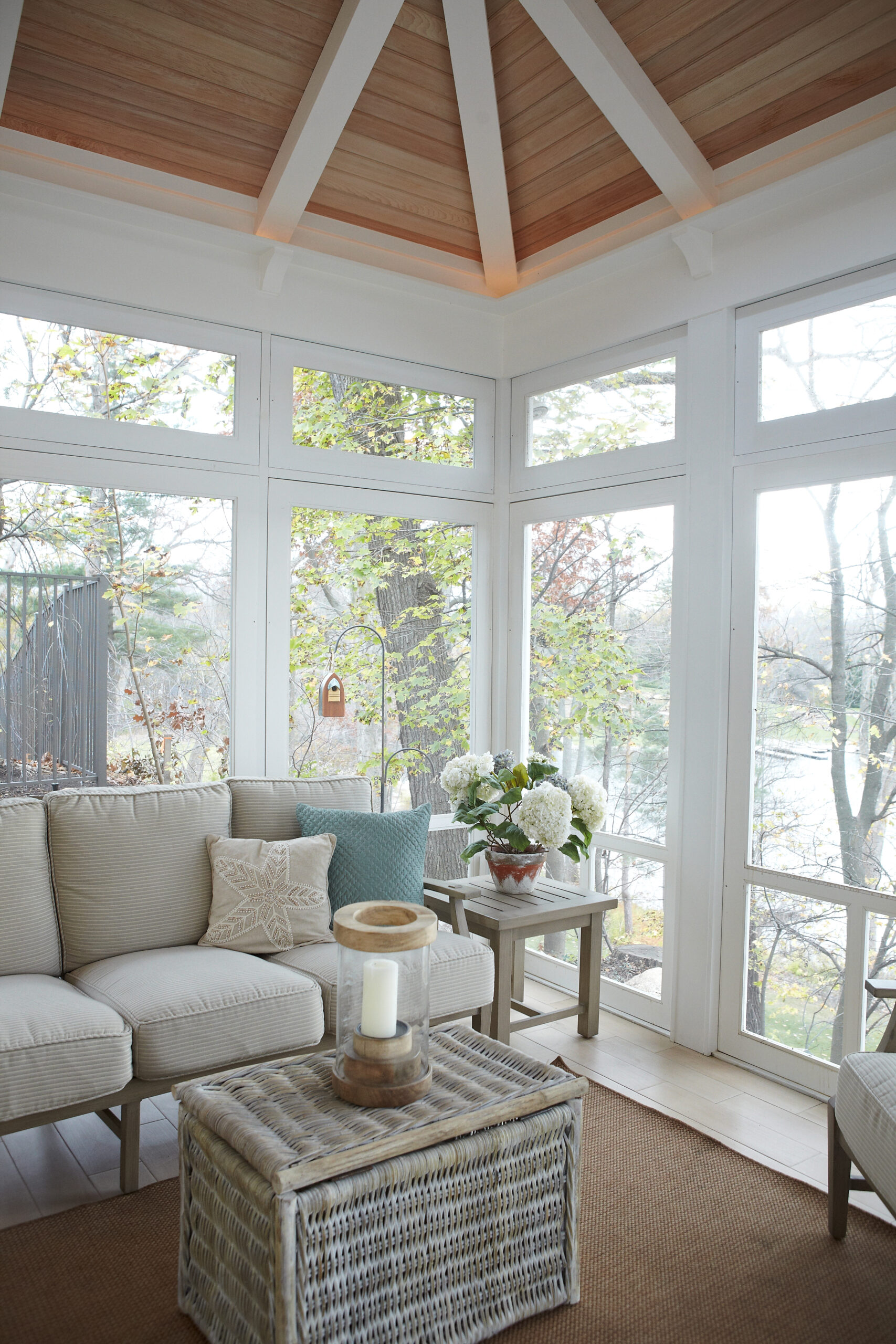 Screened porch with vaulted wood ceiling, wicker furniture, and views of surrounding trees