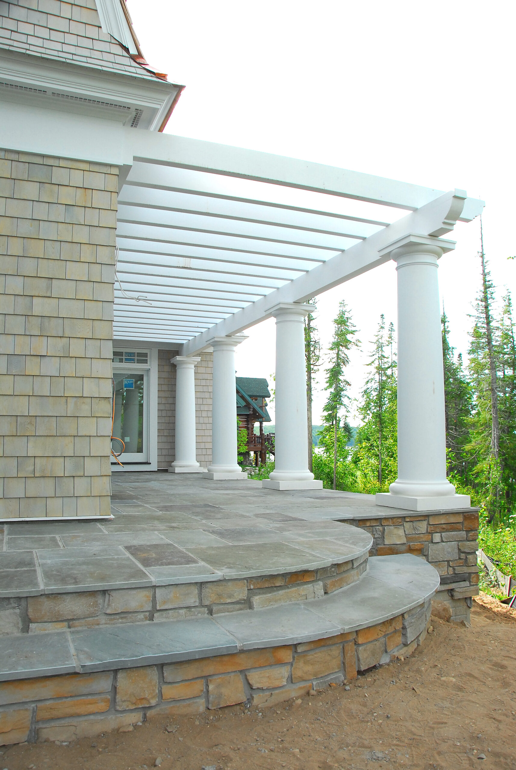 Stone patio with white pergola and round columns on lakeside home