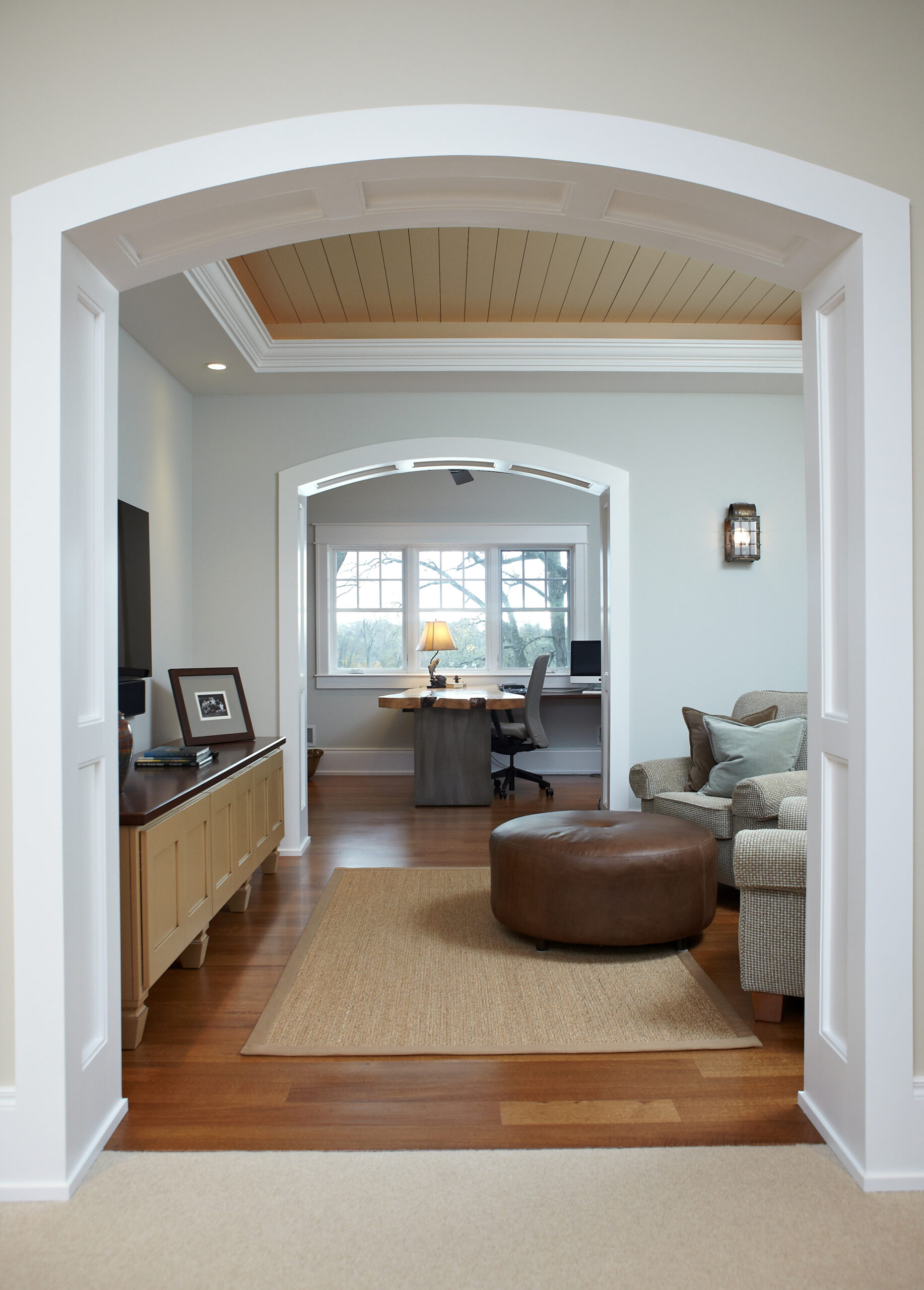 Arched interior opening leading to home office with built-in desk and warm wood floors