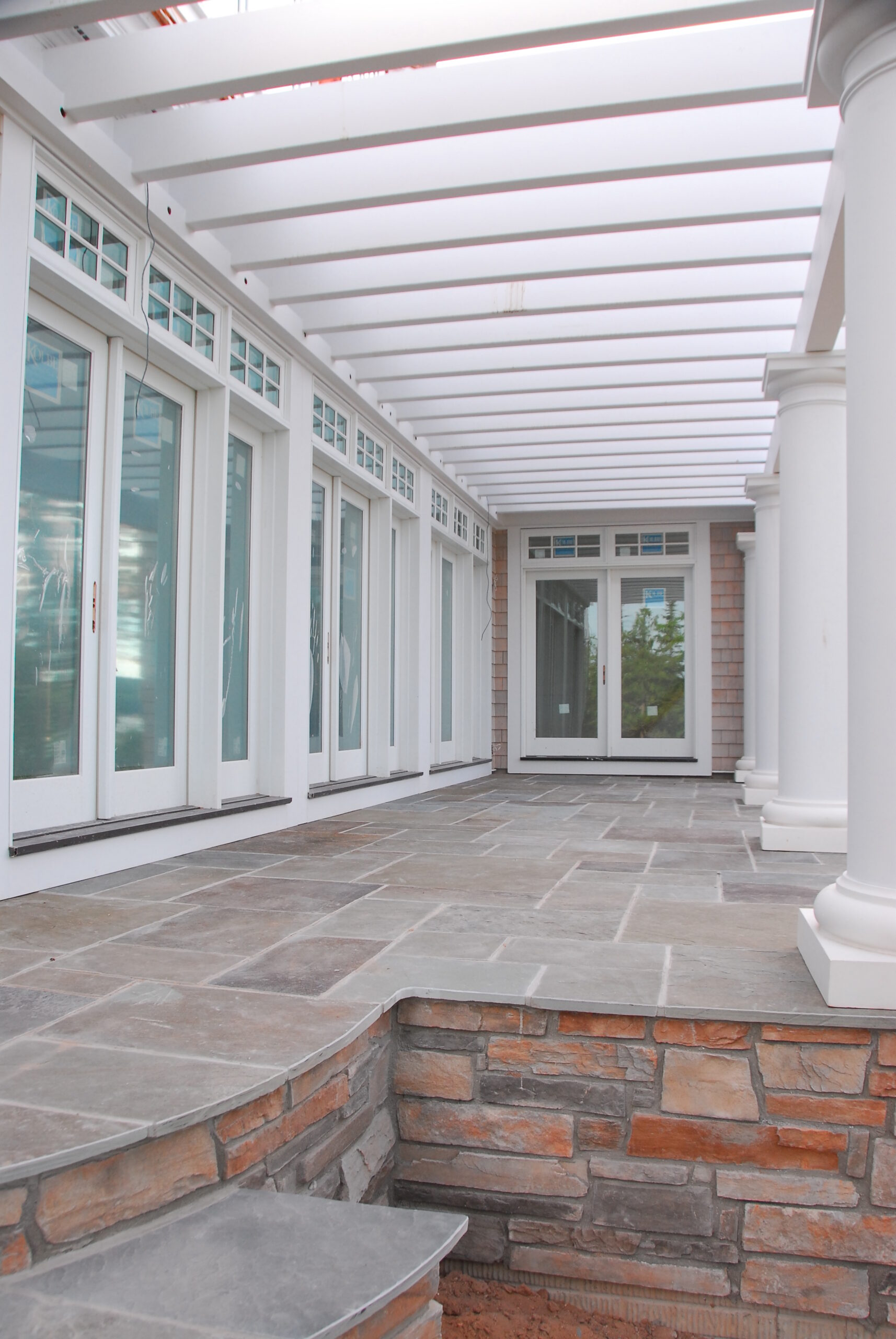 Covered stone patio with white pergola and French doors