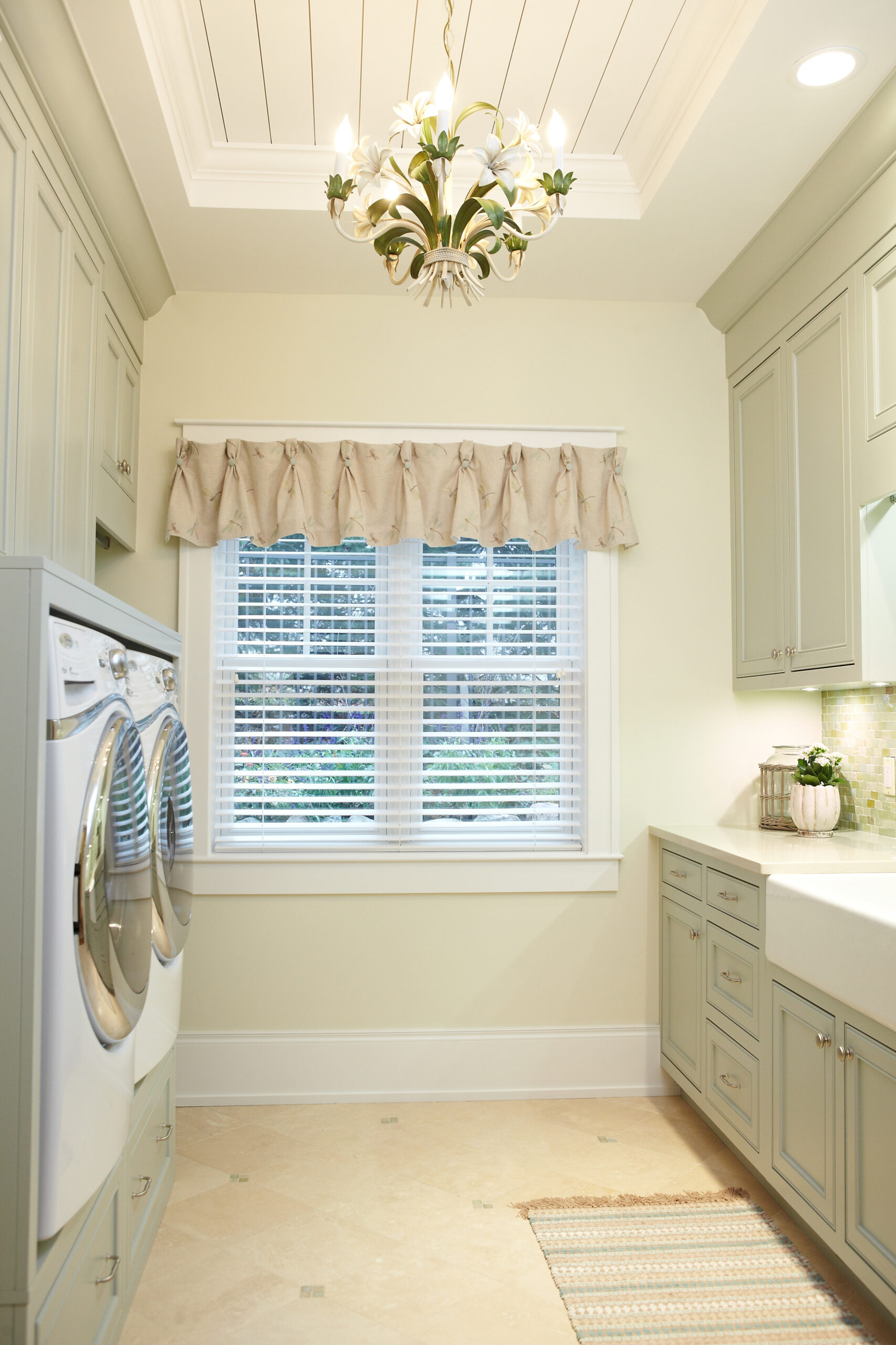 Bright cottage laundry room with built-in cabinetry, farmhouse chandelier, and front-load washer and dryer