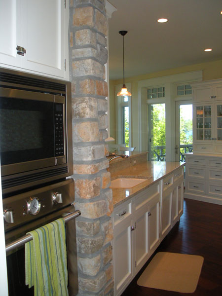 Kitchen interior with stone column, built-in oven, and long island