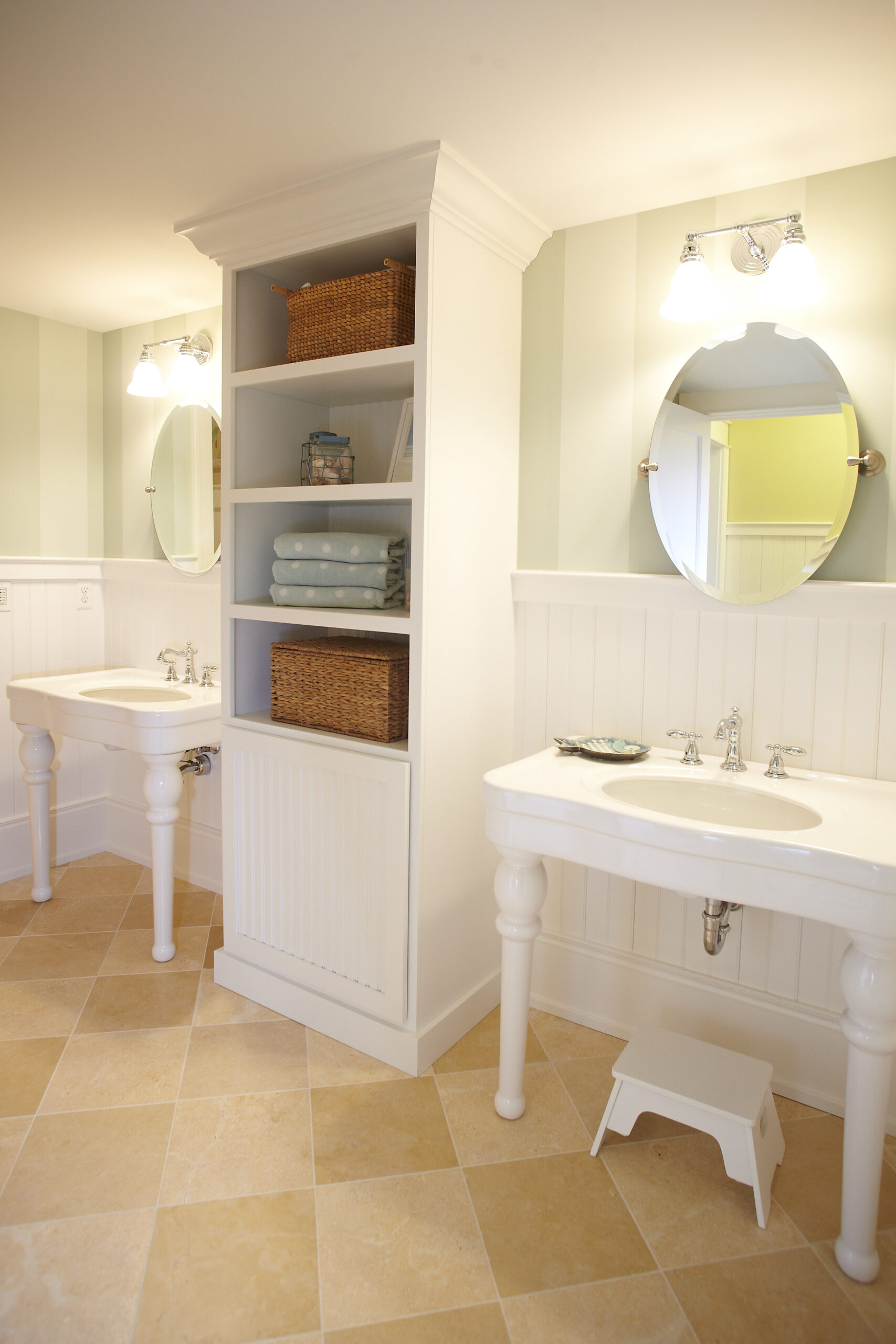 Bright cottage guest bathroom with pedestal sinks, built-in shelving, and soft striped walls