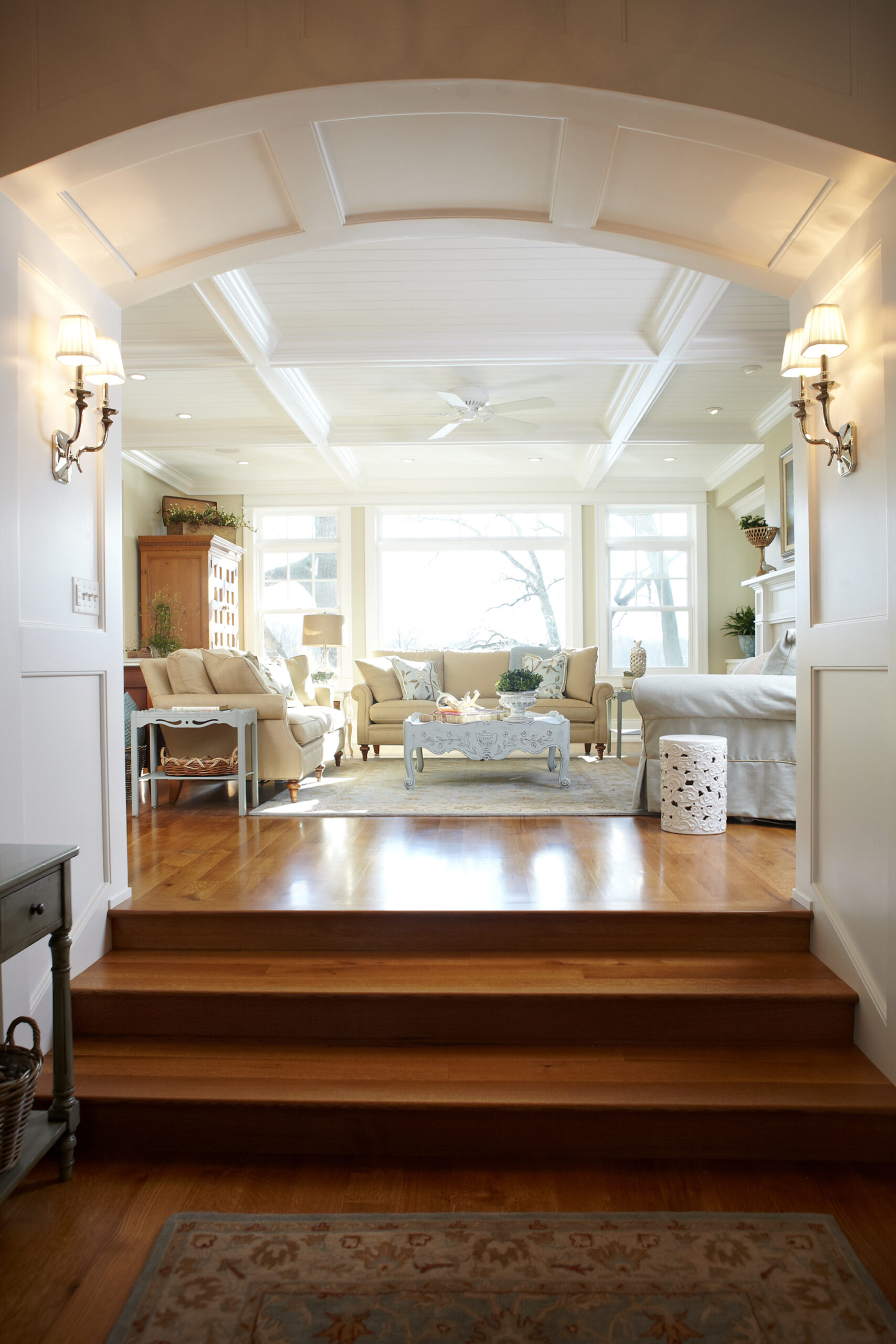 Gracious cottage entry with arched opening, hardwood steps, and sunlit living room beyond