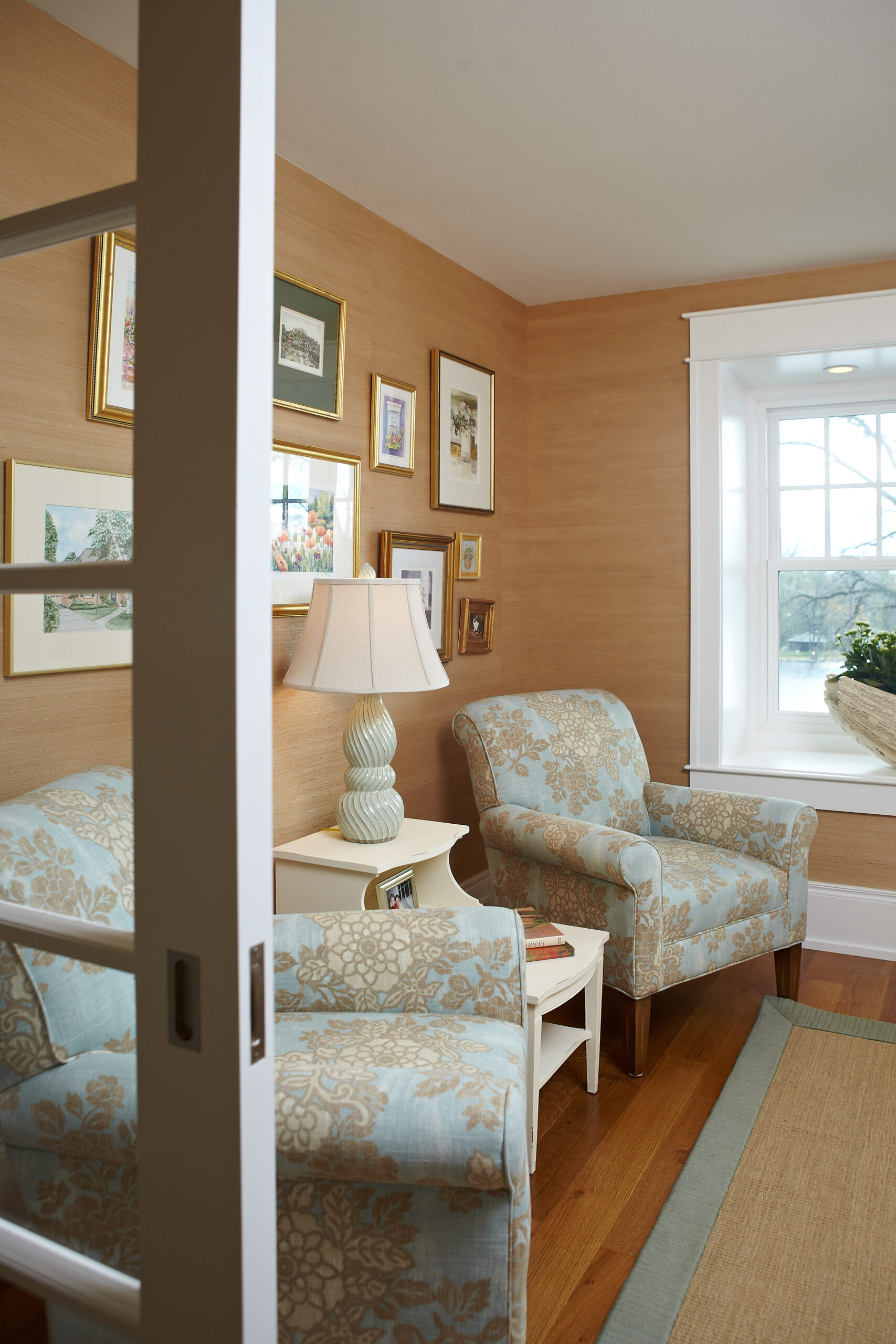Cozy cottage library with patterned armchairs, grasscloth walls, and framed artwork
