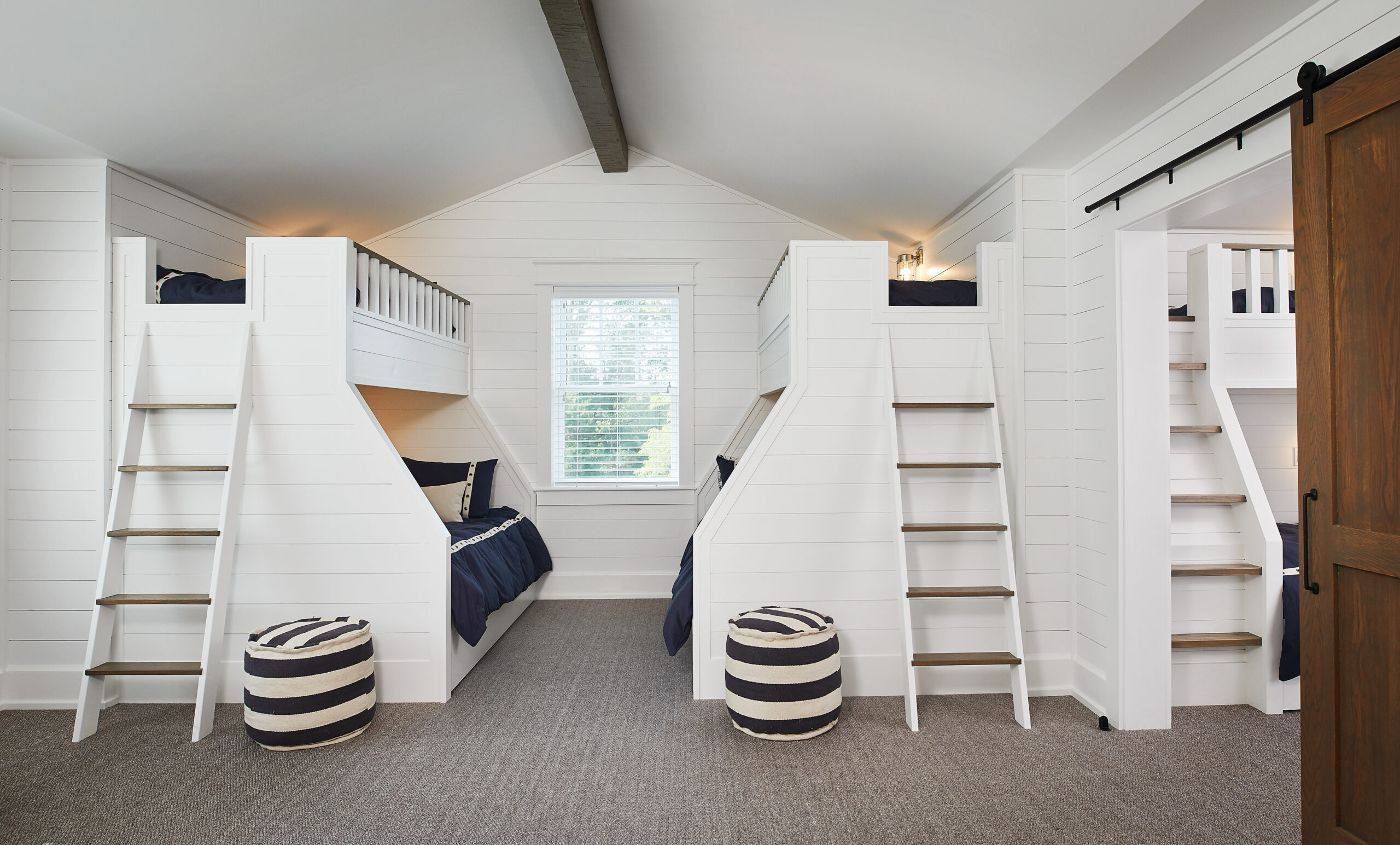 Six white custom bunk beds with built-in ladders and navy bedding in a bright, spacious room.