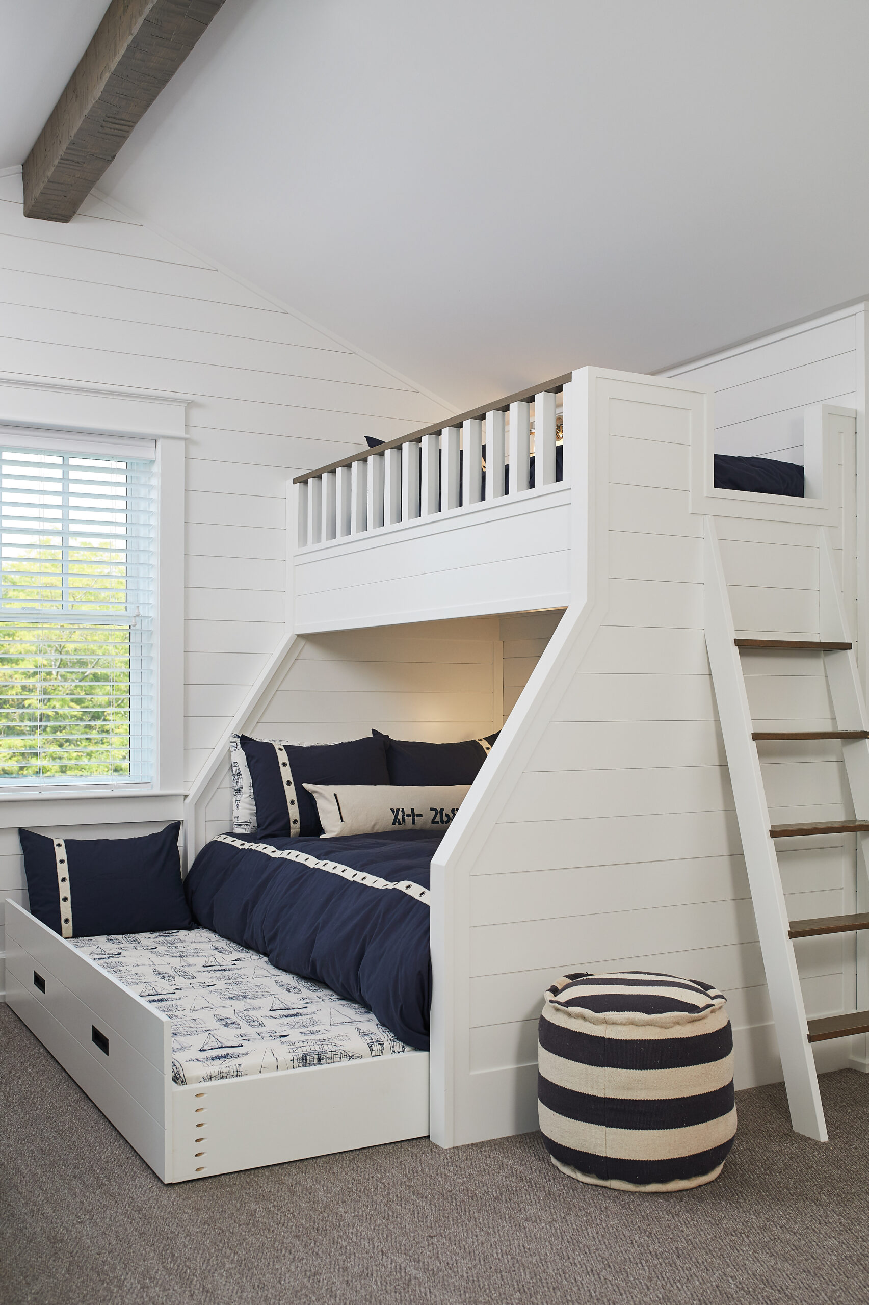 White custom bunk bed with built-in stairs, navy bedding, and a pull-out trundle bed.