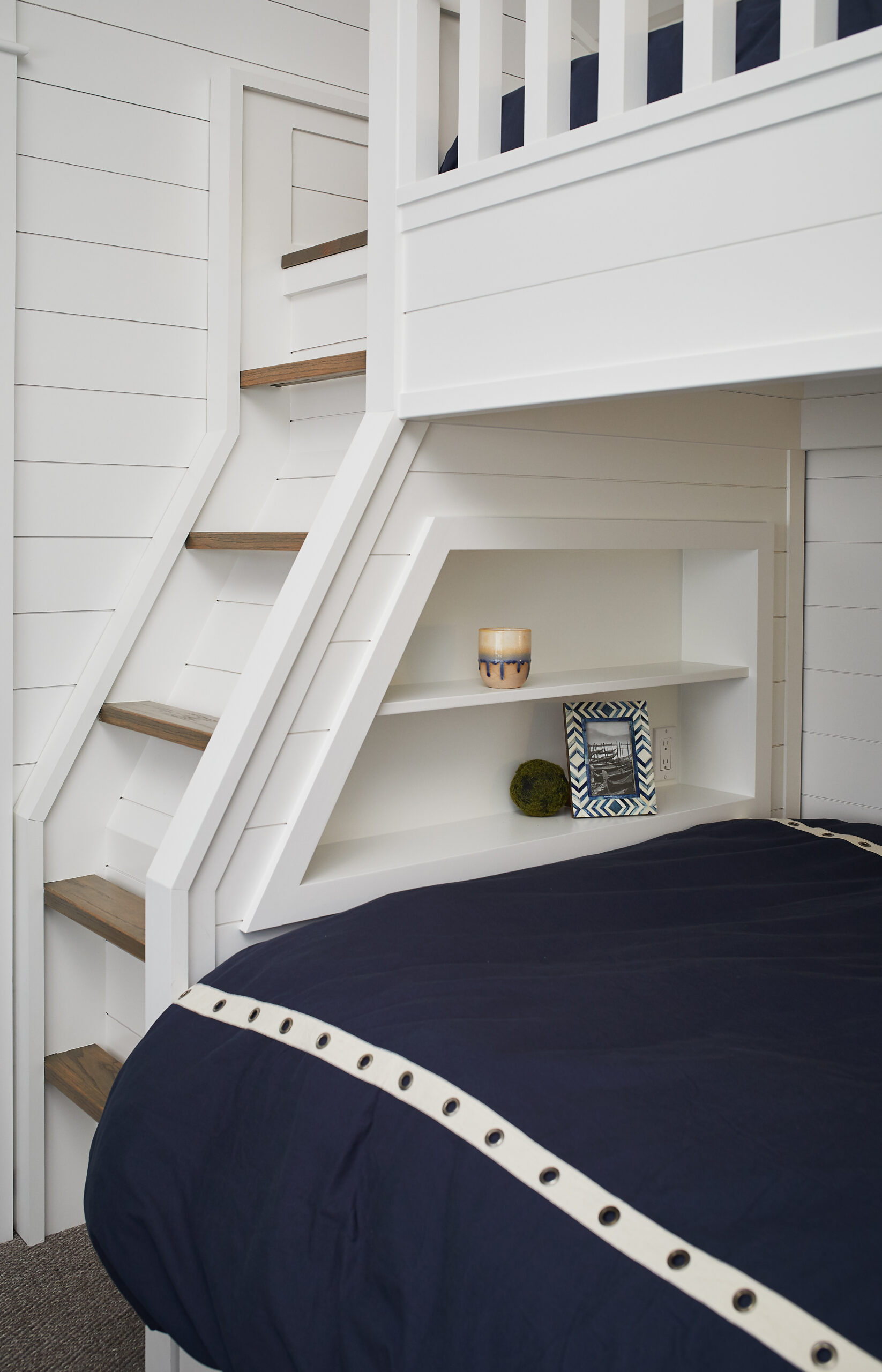 Built-in white bunk bed with natural wood steps and a cozy bookshelf nook below.