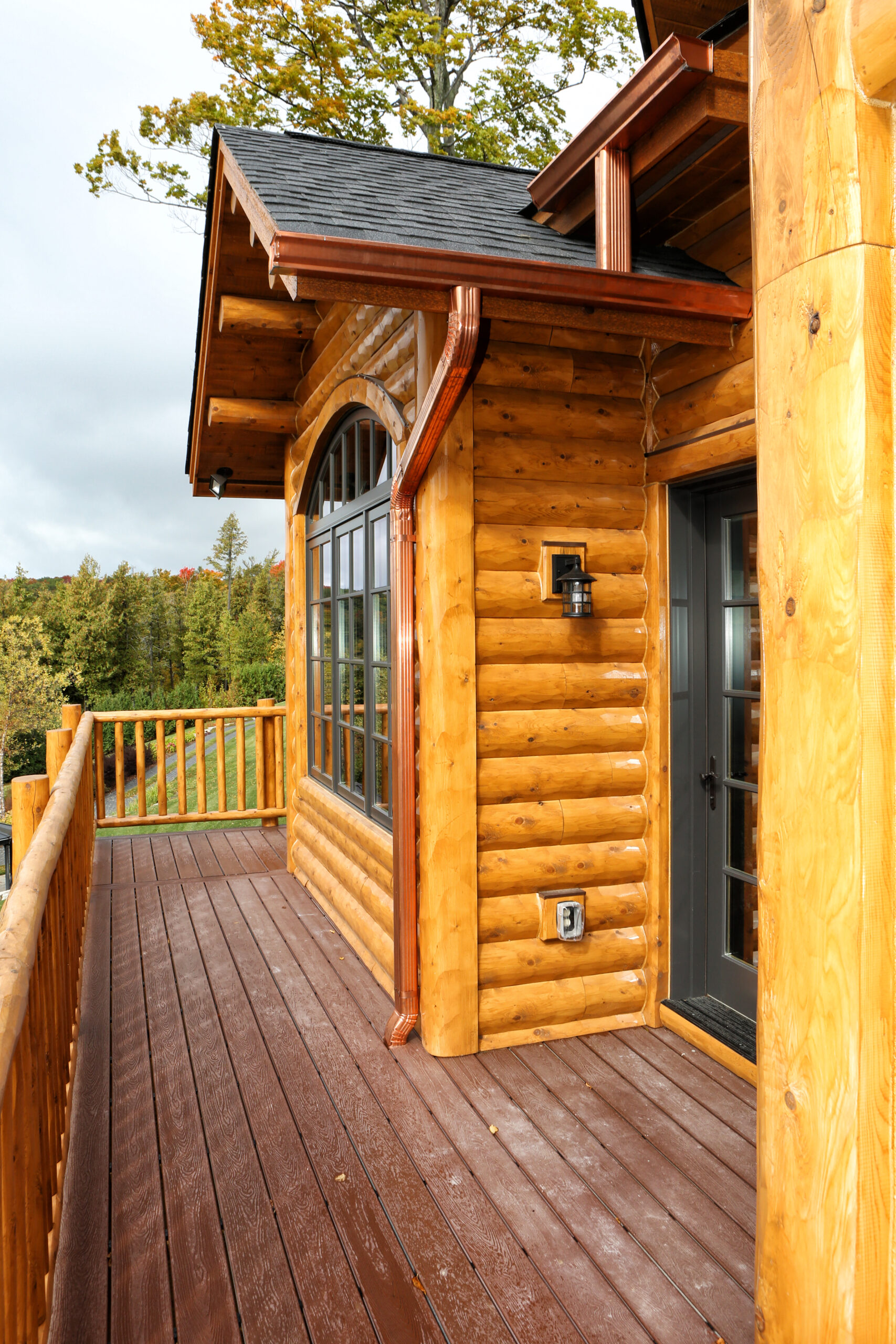 Custom log home exterior in Lake Charlevoix with arched windows, copper gutters, and elevated deck