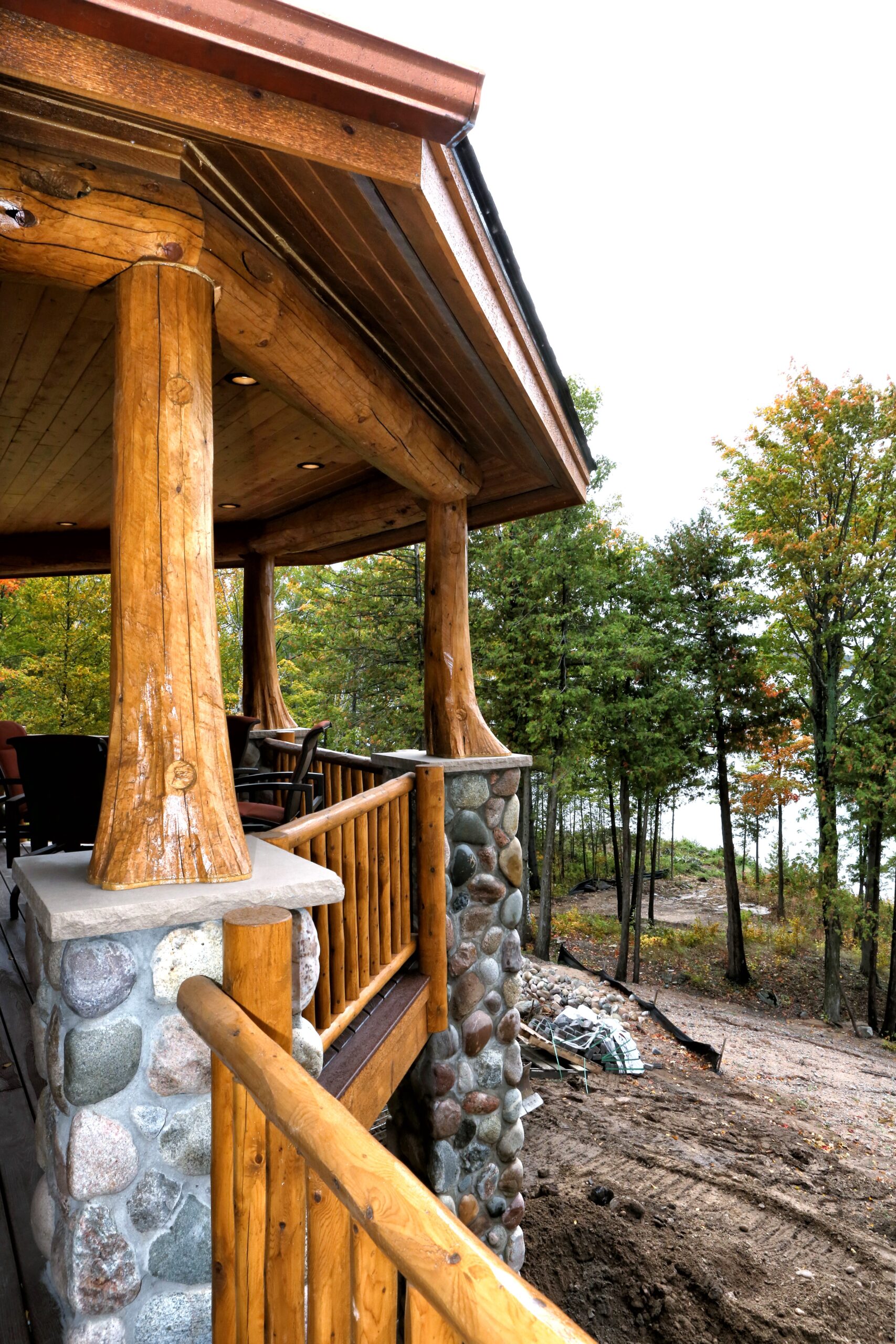 Covered porch of a luxury log home built by Eastmark Construction in Lake Charlevoix, featuring a log railing and fieldstone foundation