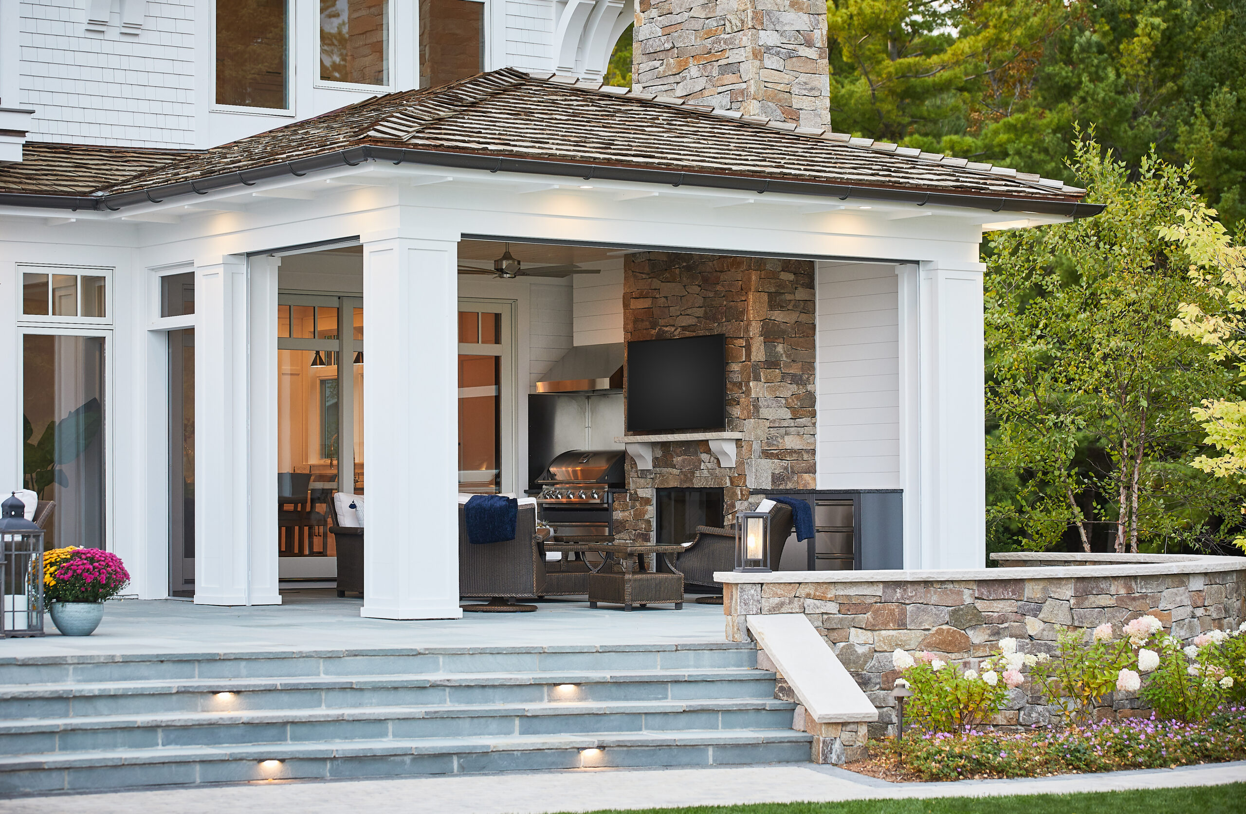 Covered outdoor living area with stone fireplace, built-in grill, and cozy seating.